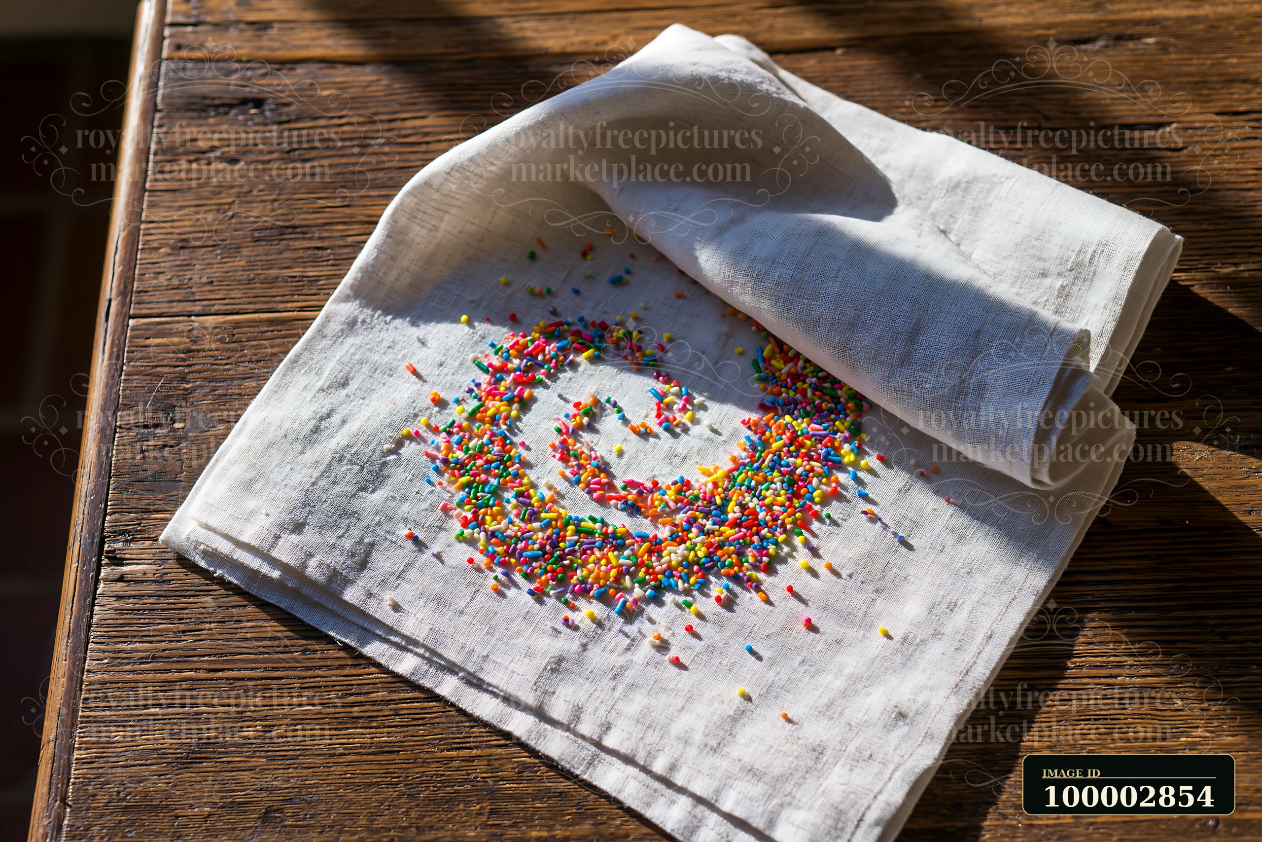 Rainbow sprinkles arranged in a swirl are spread across a linen cloth on a wooden table.