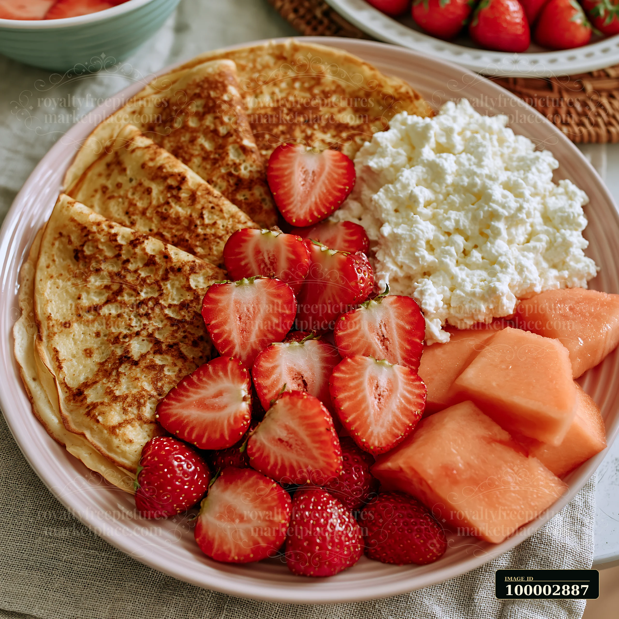 A breakfast plate with seasonal fruit features slices of fresh strawberries and diced cantaloupe alongside fluffy pancakes and a serving of cottage cheese.