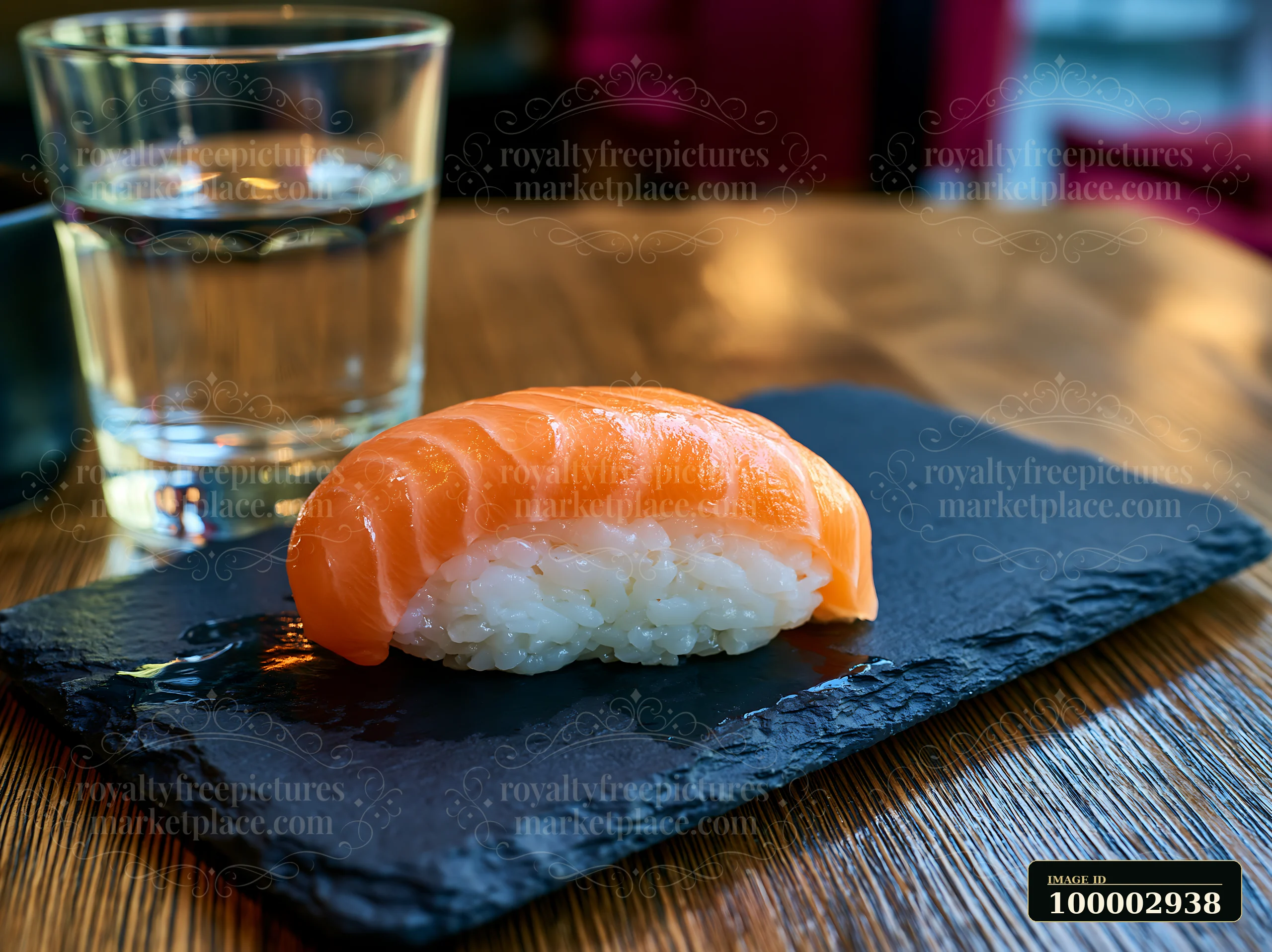 One salmon nigiri on slate plate is presented with a glass of water in a casual dining setting.