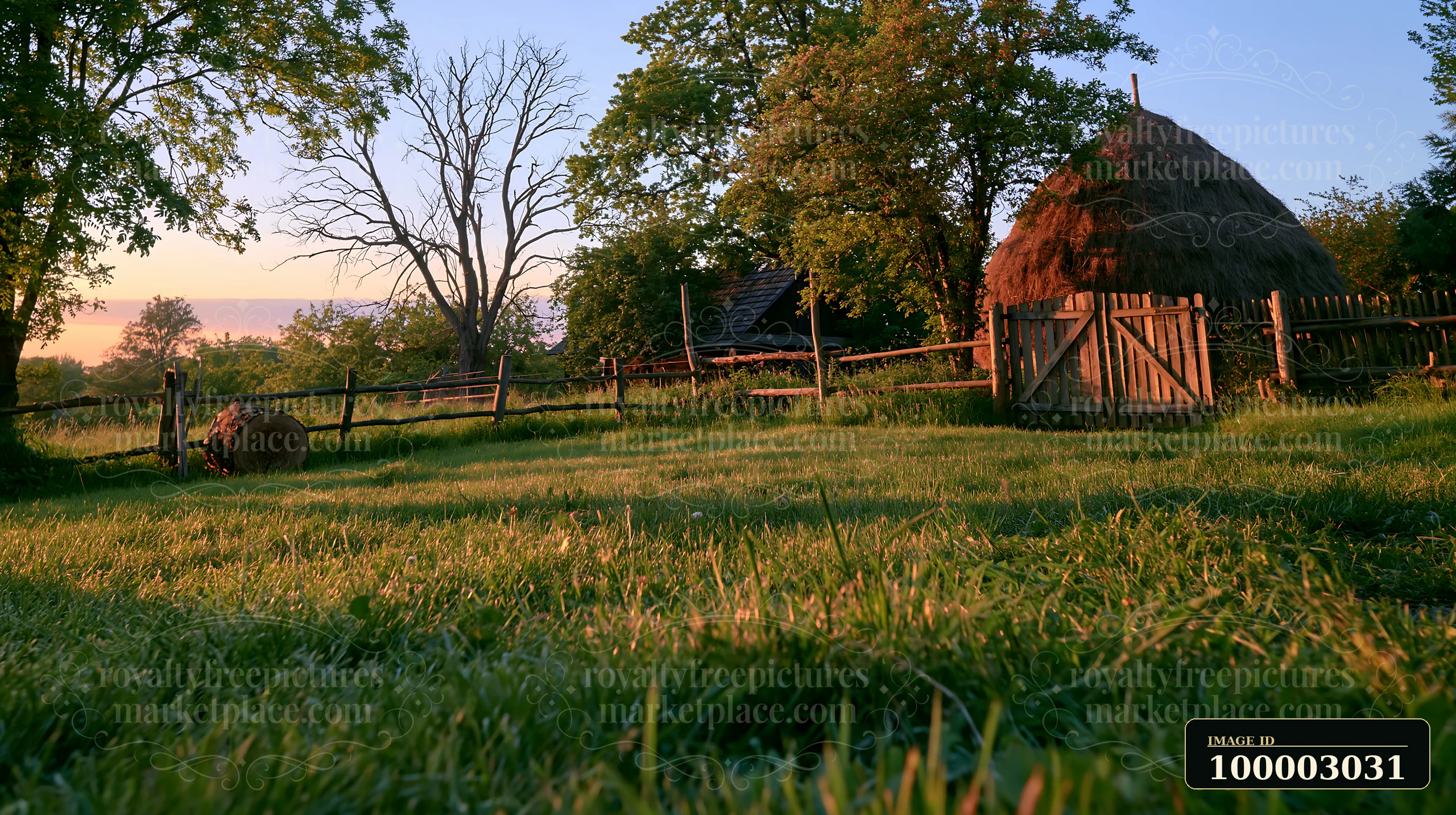 A traditional haystack stands in a meadow at sunset, surrounded by trees and a wooden fence.