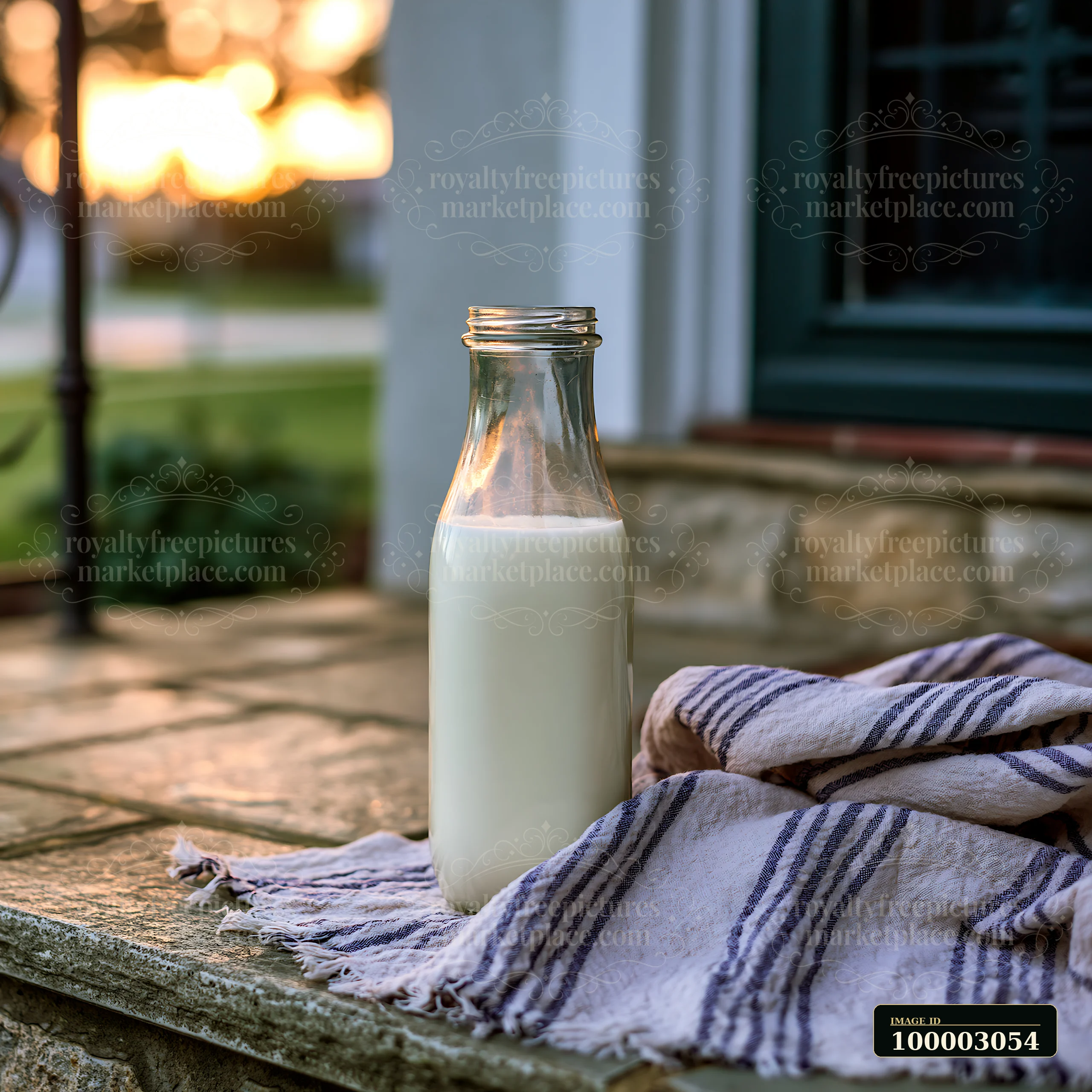 Glass milk bottles on a doorstep at sunrise sit next to a striped cloth.