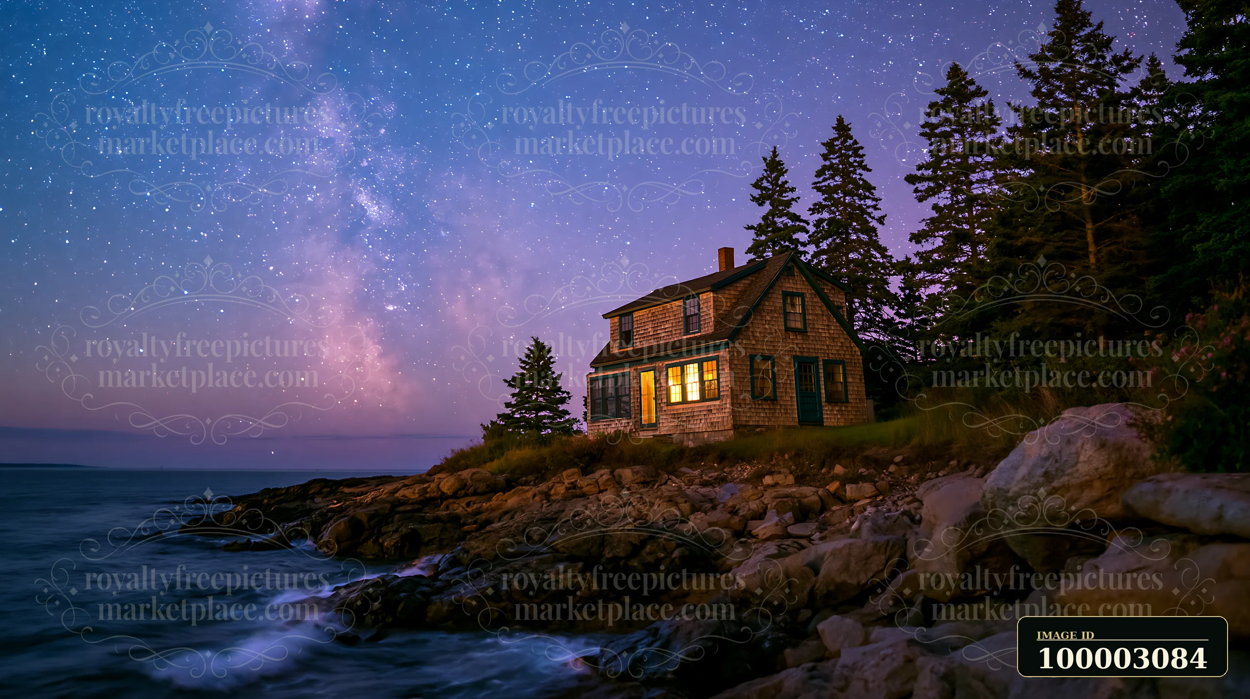 A house sits on the rocky shore with a radiant night sky filled with stars above.