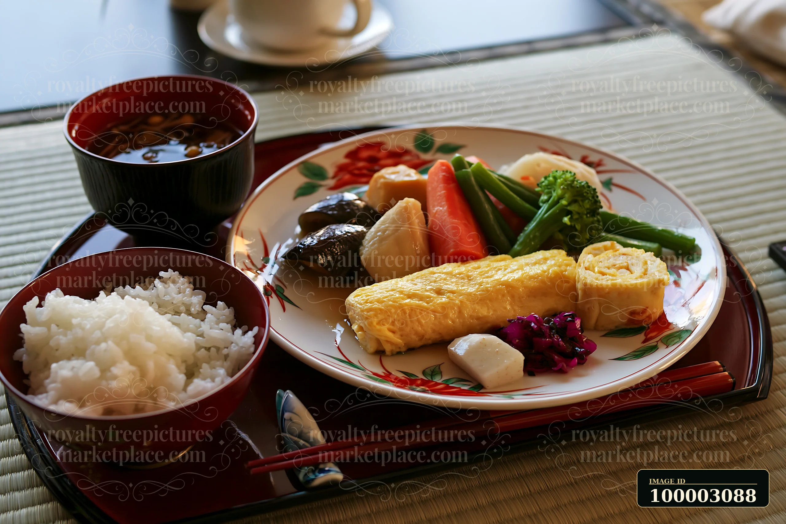 This breakfast plate with Japanese breakfast includes rice, a rolled omelet, steamed vegetables, and soup, served on a decorative tray in a traditional dining s