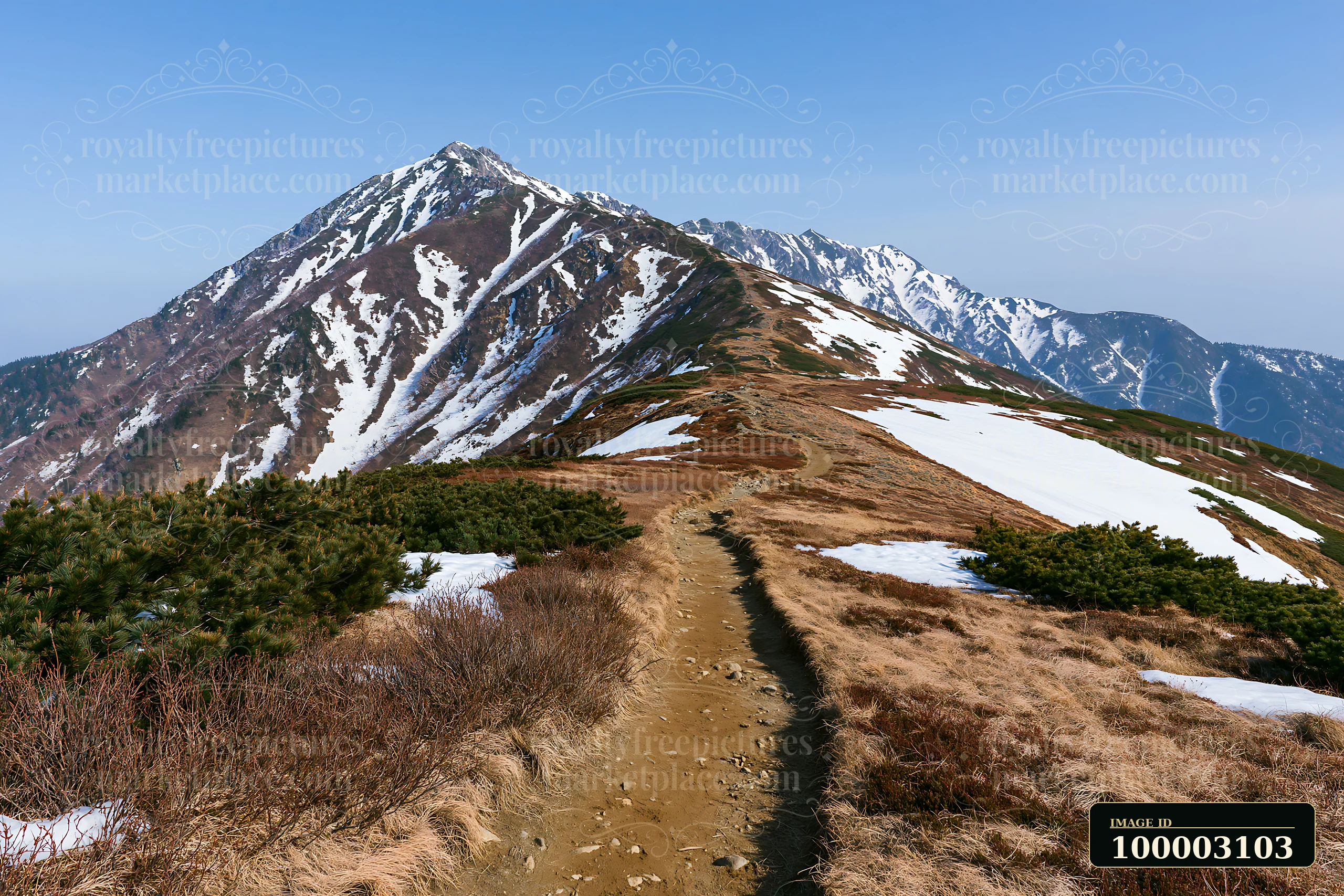A hiking trail leads along a high mountain ridge with snow patches.