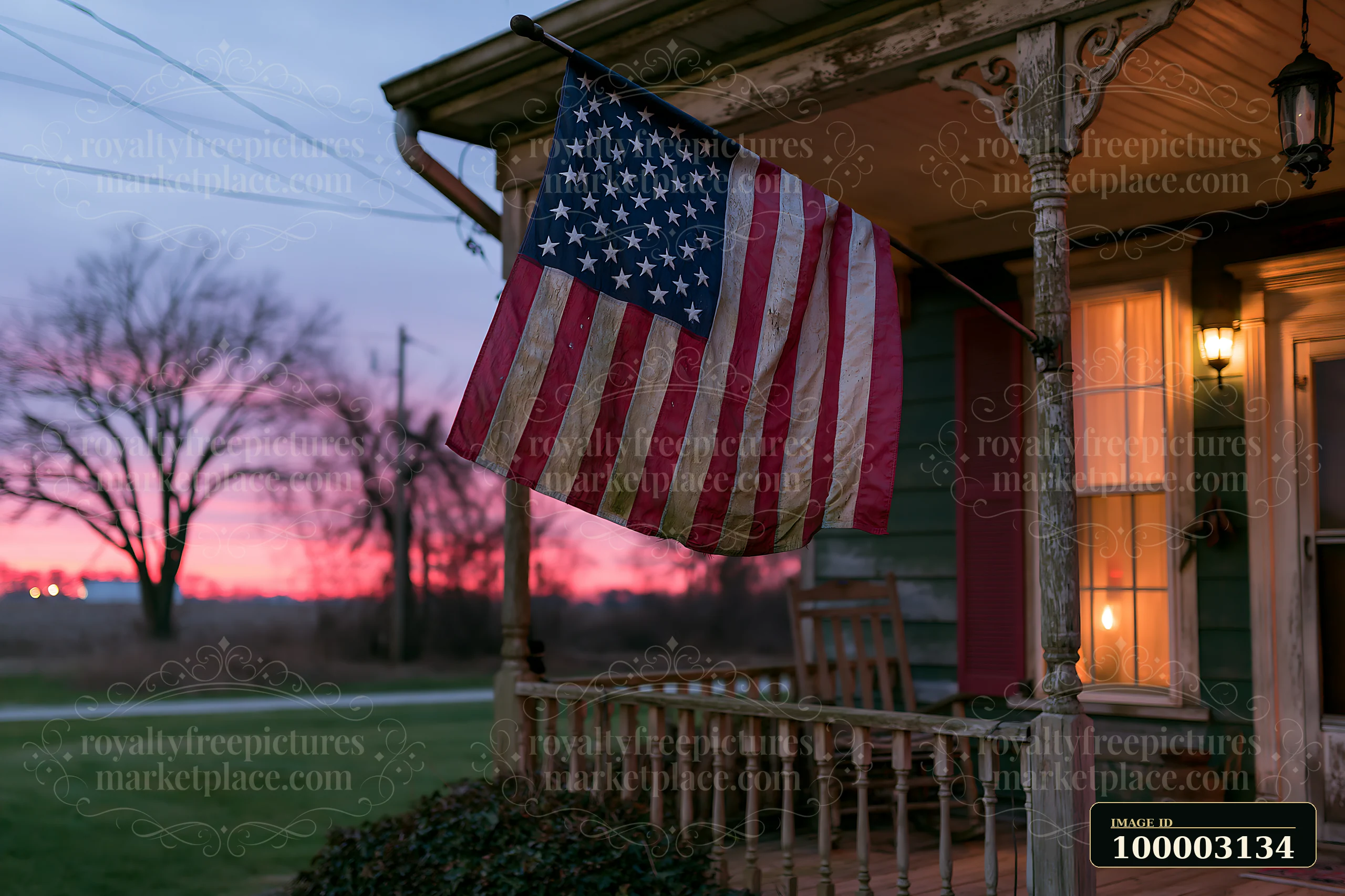 The American flag on a rural farmhouse waves gently in the evening breeze near a porch.