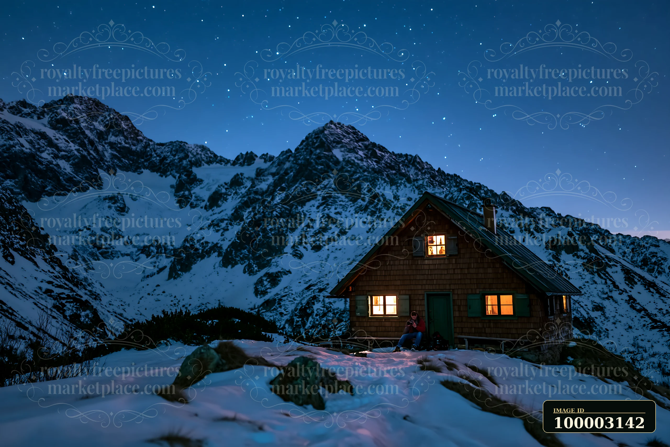 A photographer sits outside a cabin in the mountains, capturing starry skies above snow-covered peaks during the night.