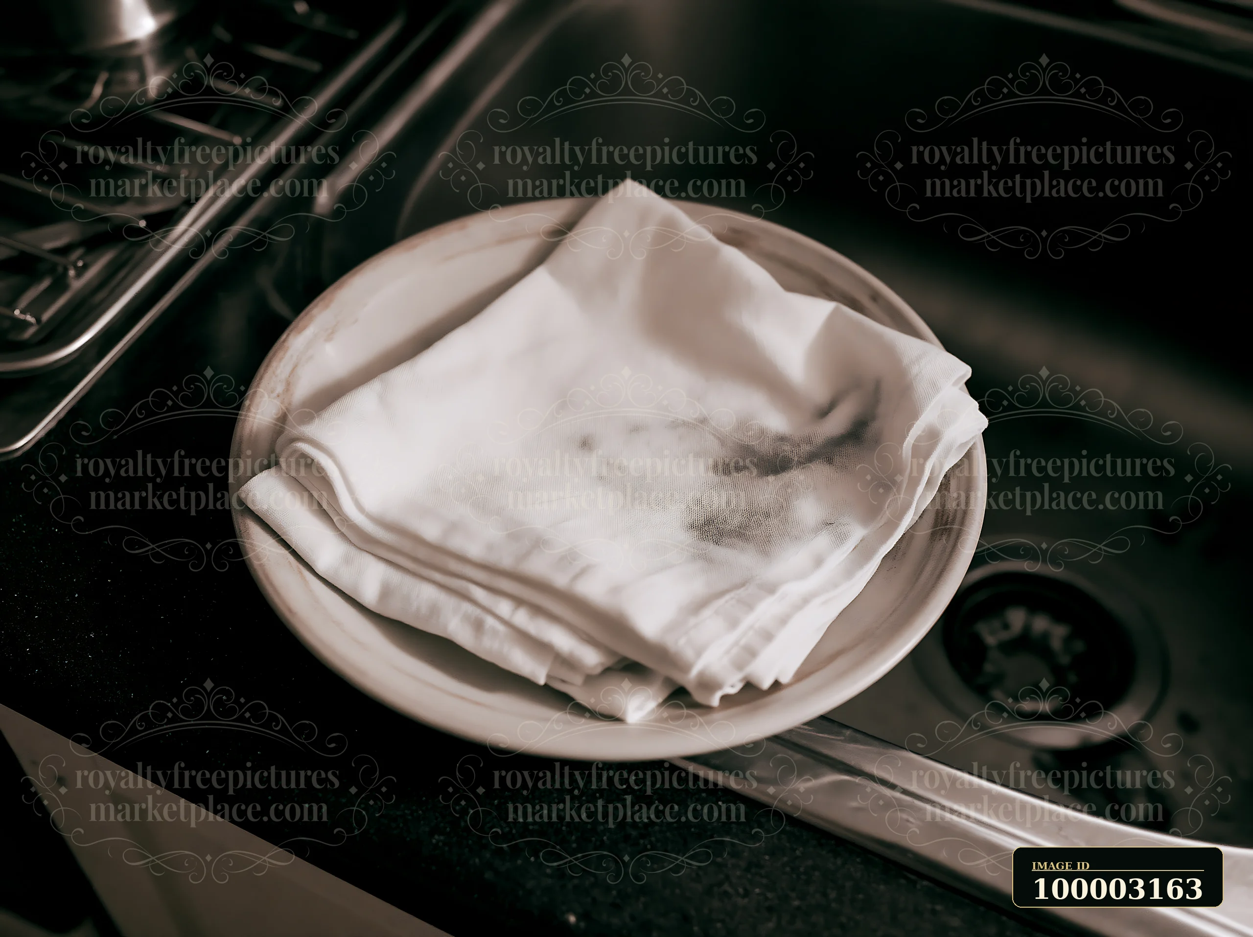 A stack of white cloth napkins shows accidental ink splashes resting on a round dish near a sink.