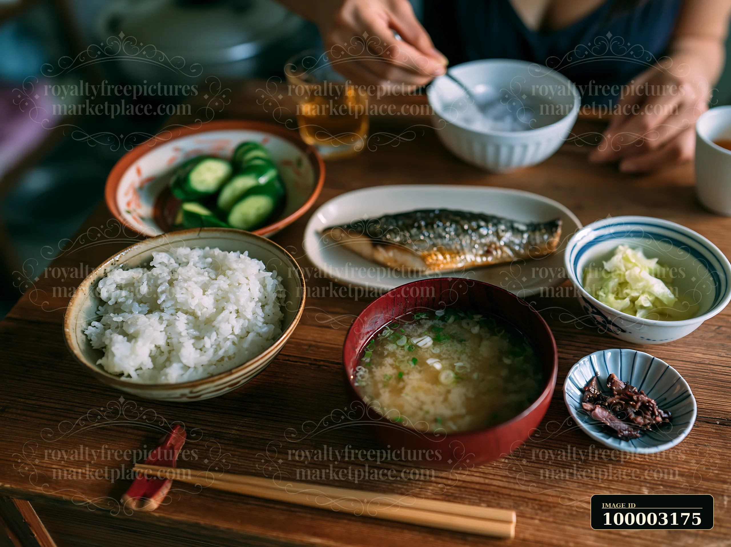A person enjoys a traditional sushi breakfast in Japan, featuring rice, miso soup, grilled fish, cucumber, and pickled vegetables.