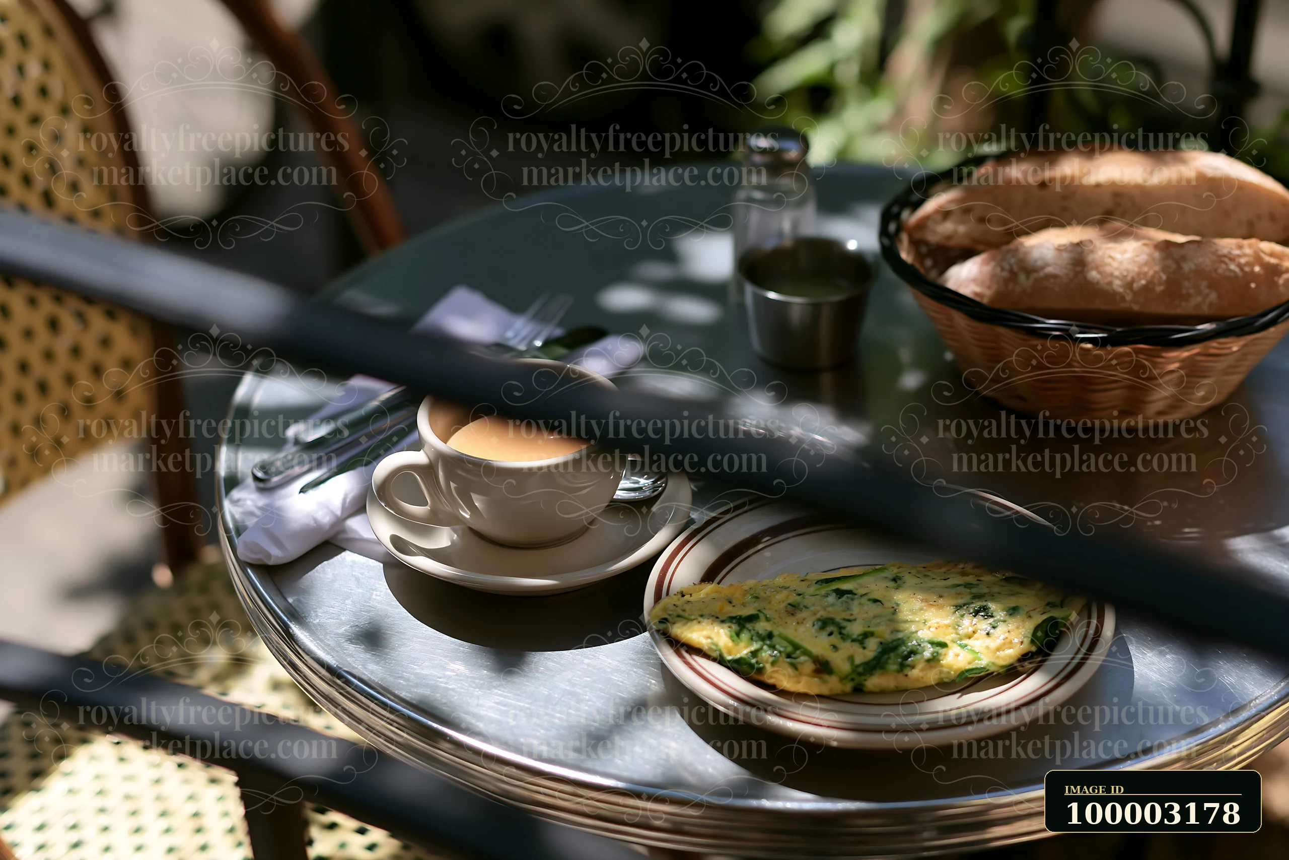 A street cafe table displays a cup of milk coffee beside a plate with an omelet and a basket of bread.