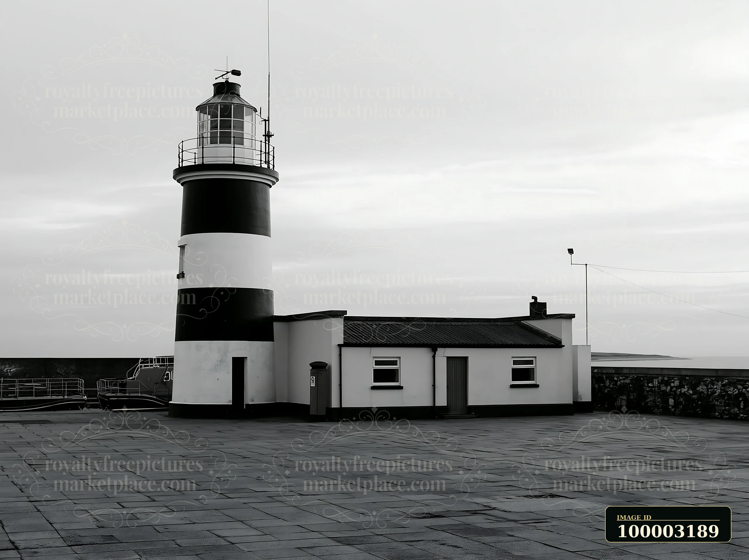 A lighthouse with black and white stripes stands near the ocean on a cloudy day.