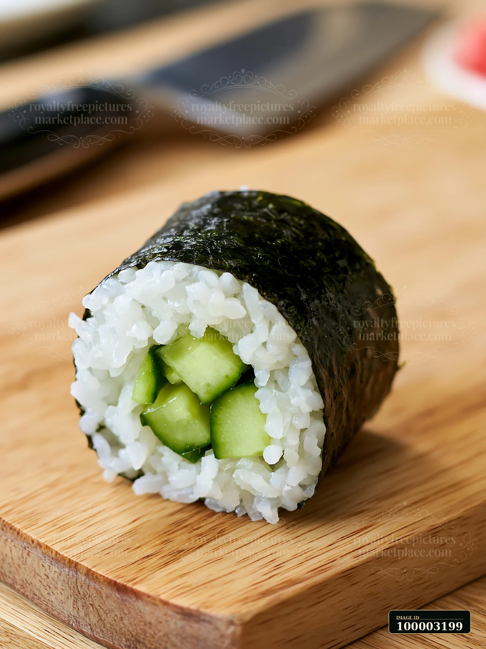 A single cucumber maki roll sits on a wooden cutting board with a knife nearby.