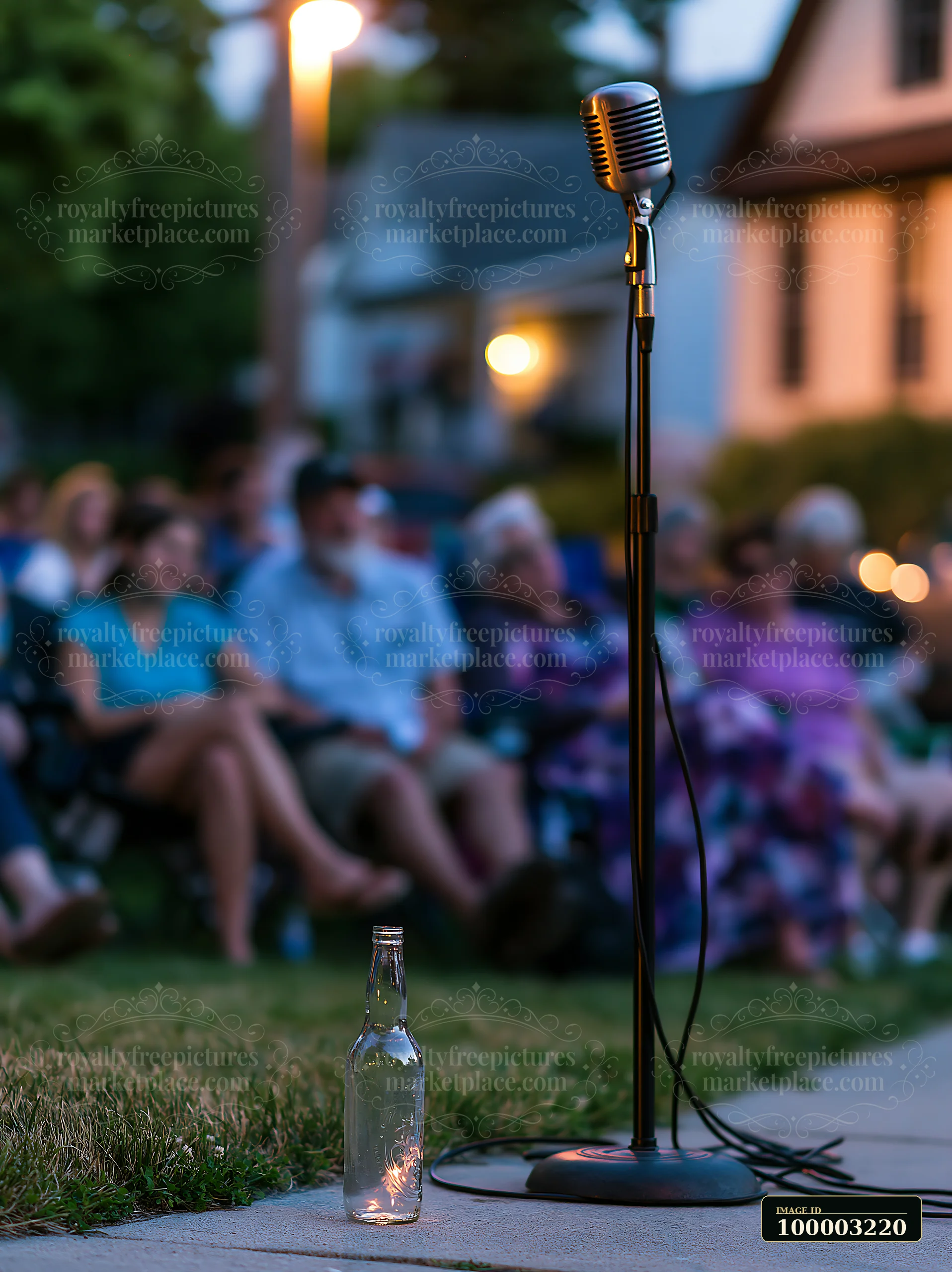 An empty bottle sits on the ground next to a microphone at an outdoor event in the evening.