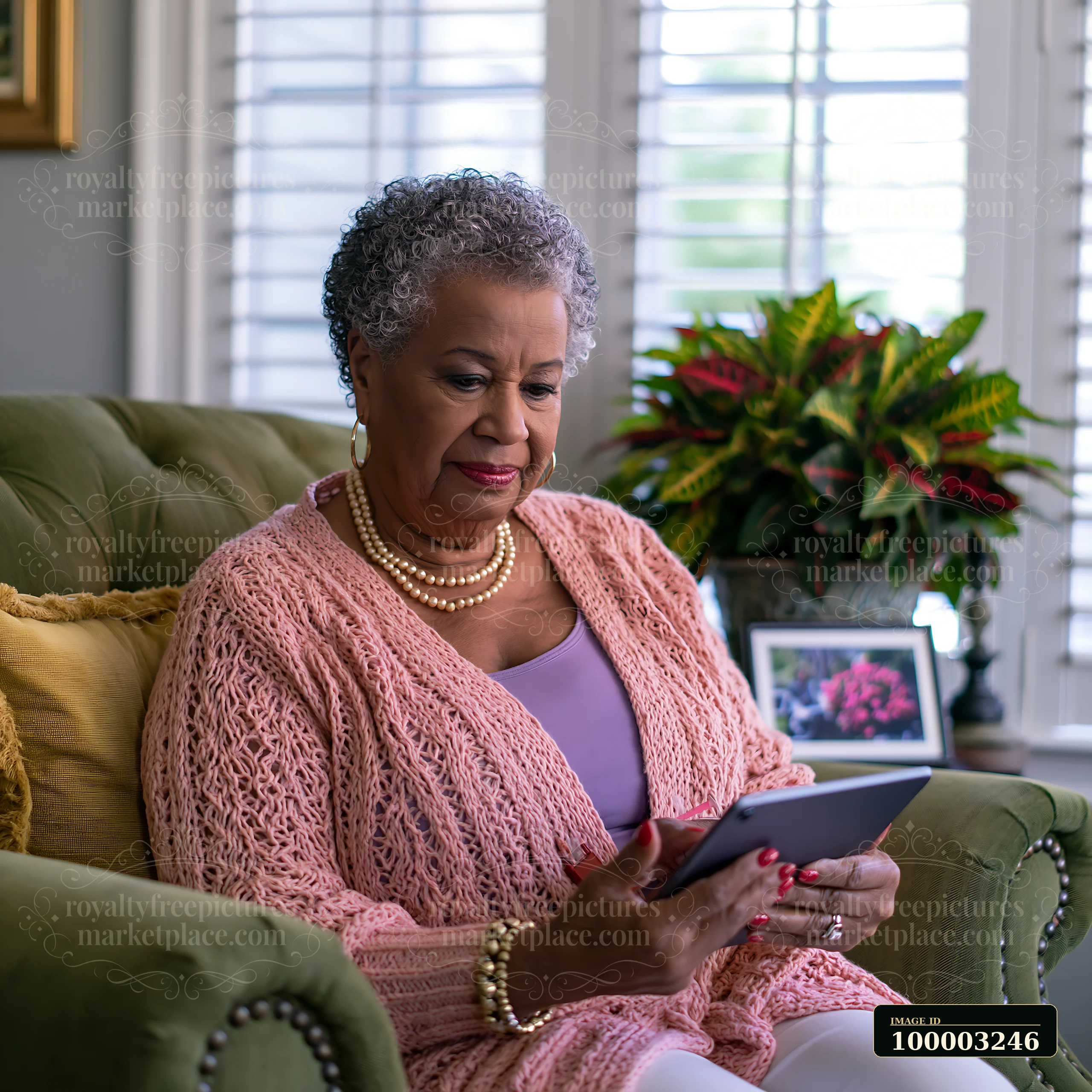 A woman with Parkinson's sits comfortably on a green couch while using a tablet.