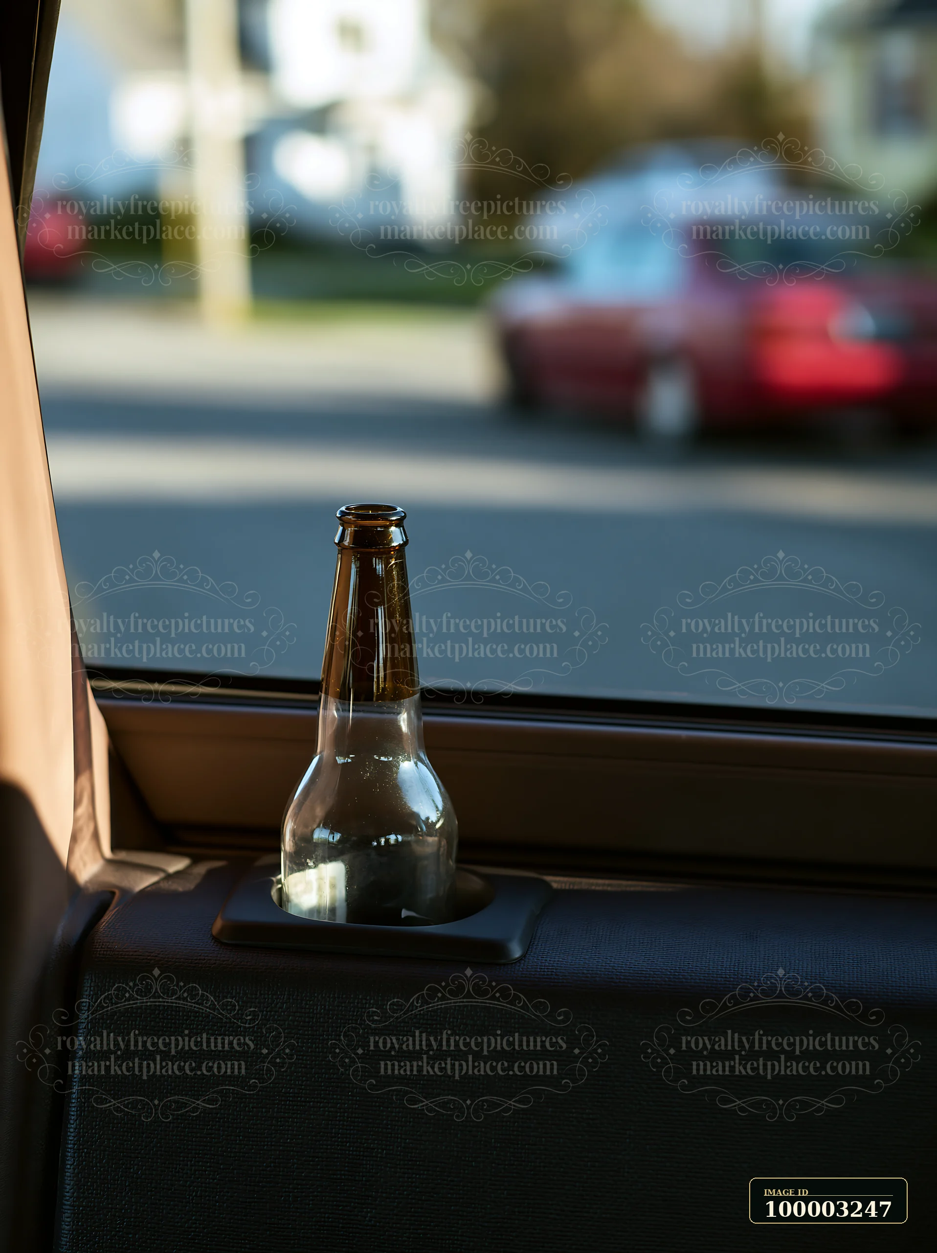 A clear glass bottle rests in the cup holder of a car.
