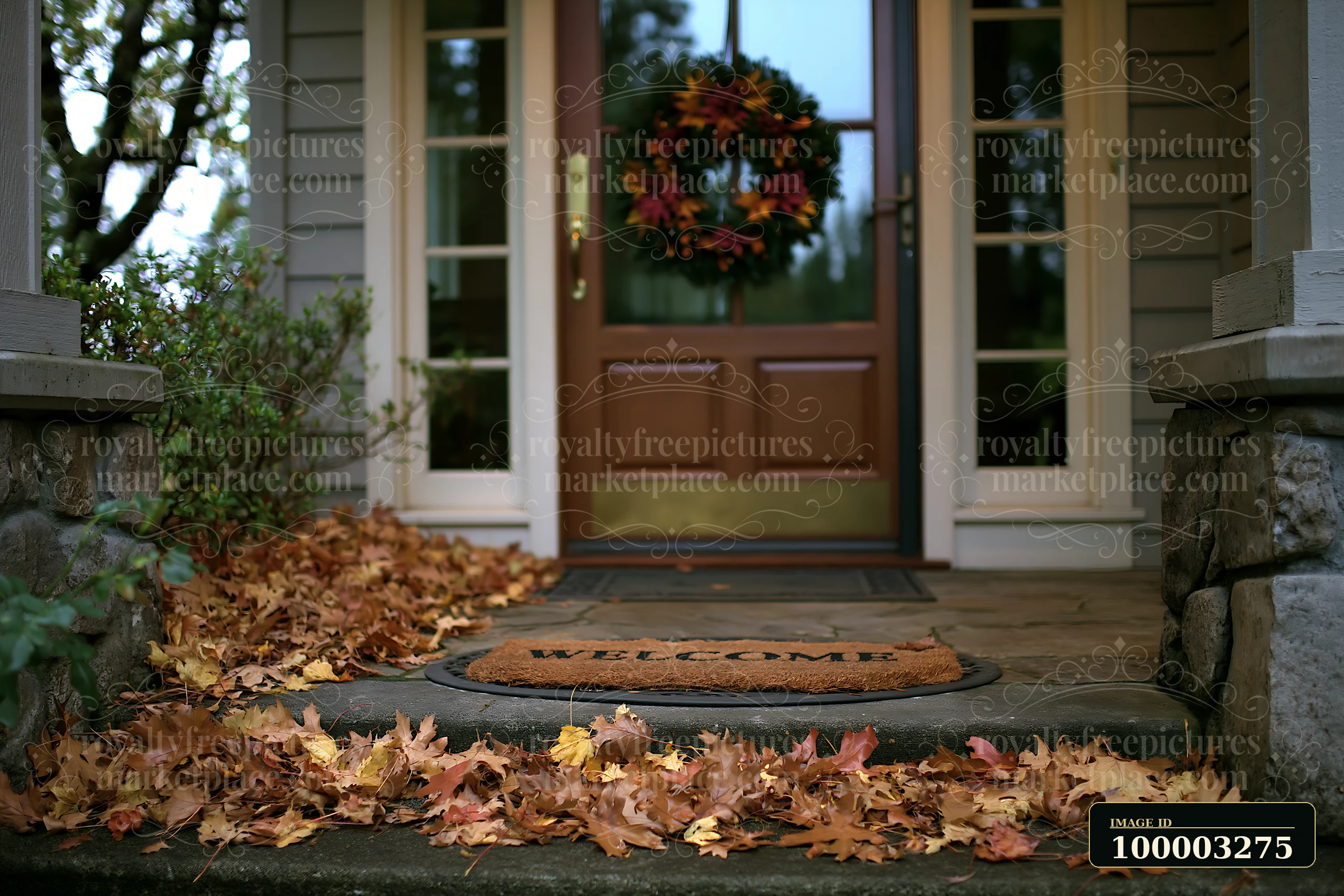A glass front door with a wreath welcomes visitors at a home entrance covered in autumn leaves.