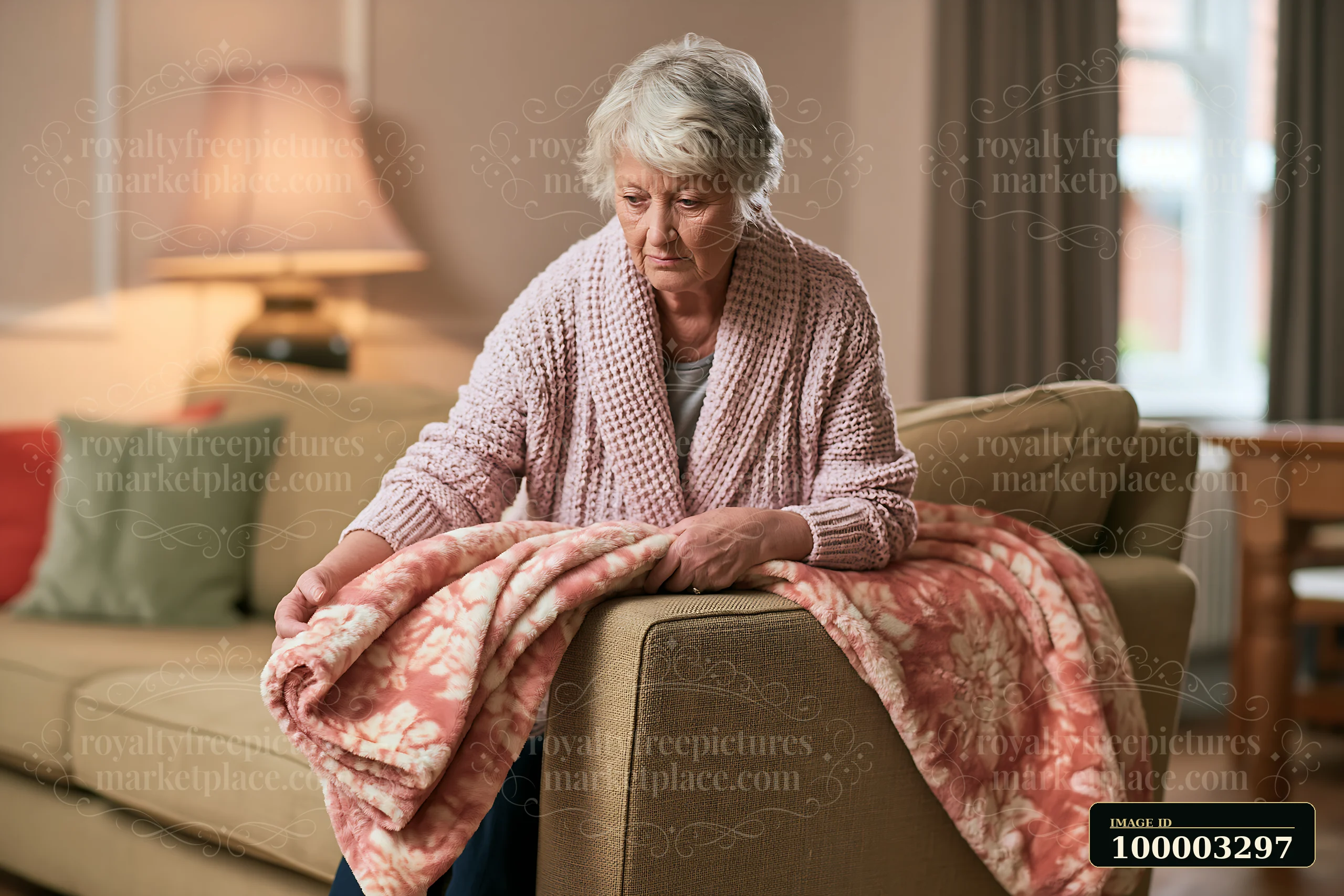 An elderly woman with dementia participating in daily activities sits on a couch, adjusting a pink blanket.