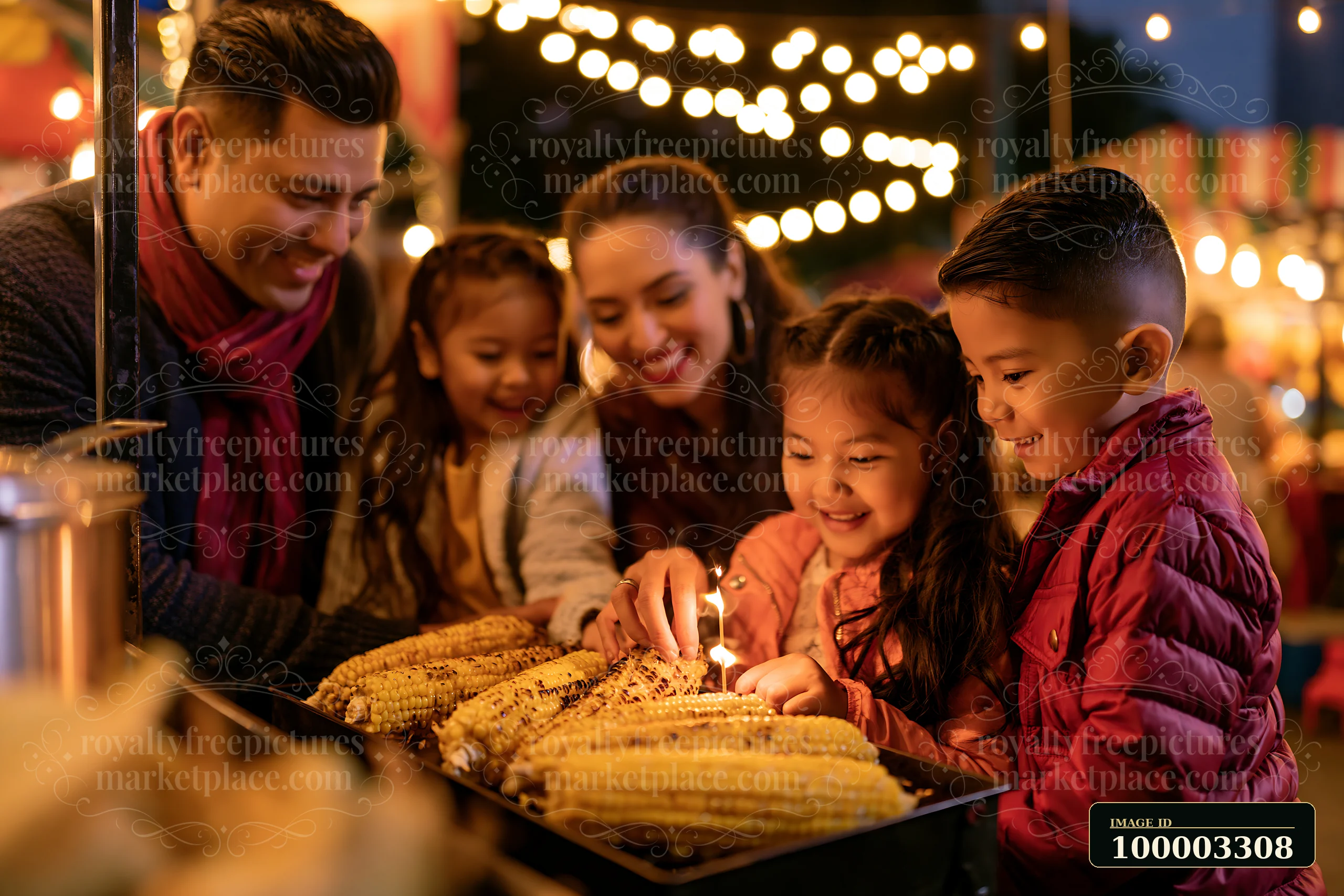 A family at food stalls lights a candle while gathering near roasted corn at a lively night market.