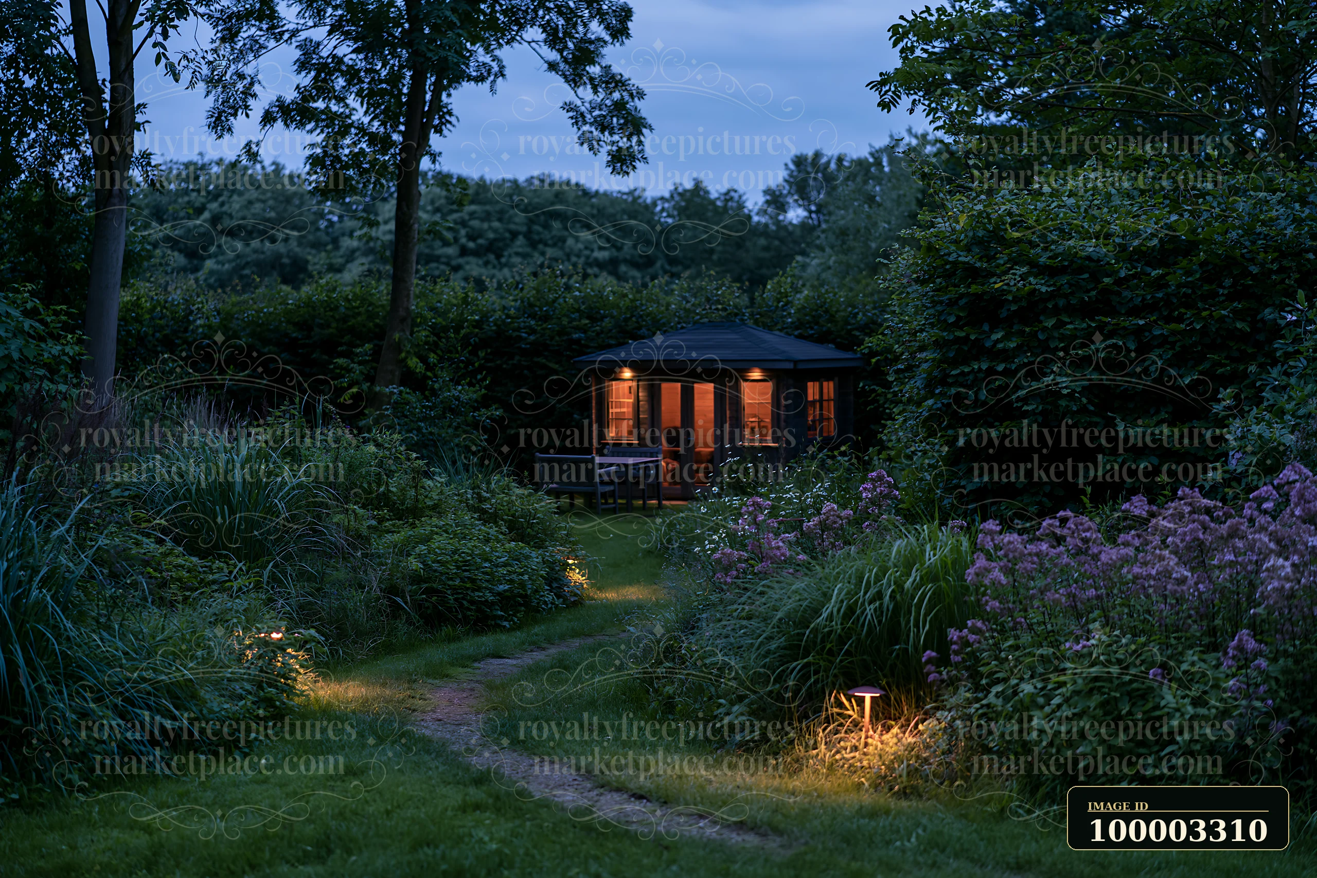 The garden studio sits illuminated at dusk, surrounded by lush greenery and flowers.