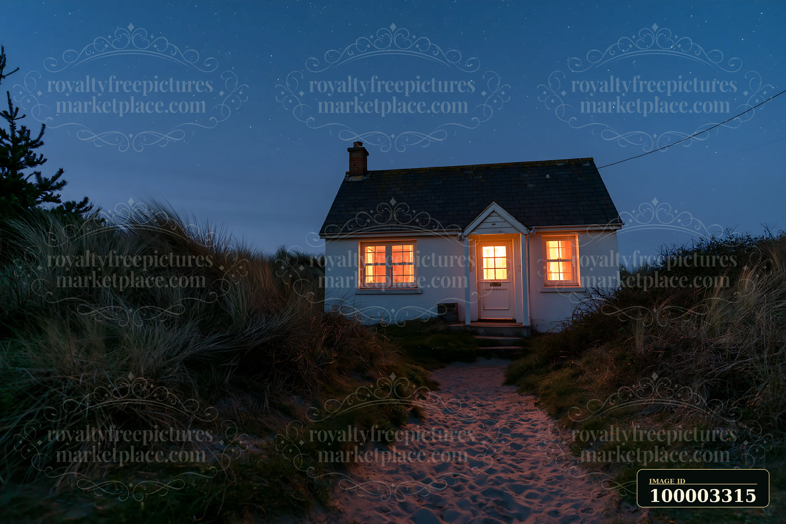 A coastal cottage stands amid sand and grass at night.