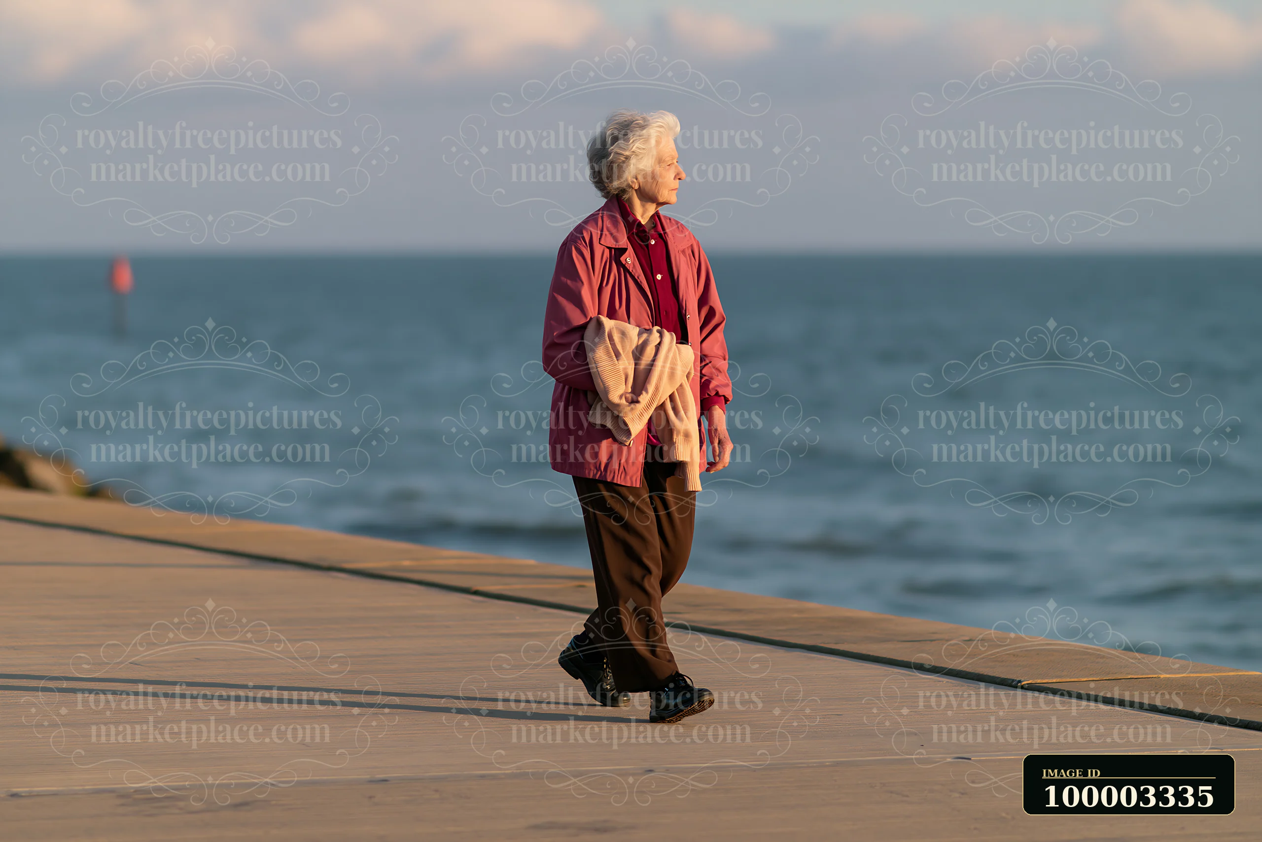 An elderly woman with Parkinson's disease walking outdoors along a pathway near the water.