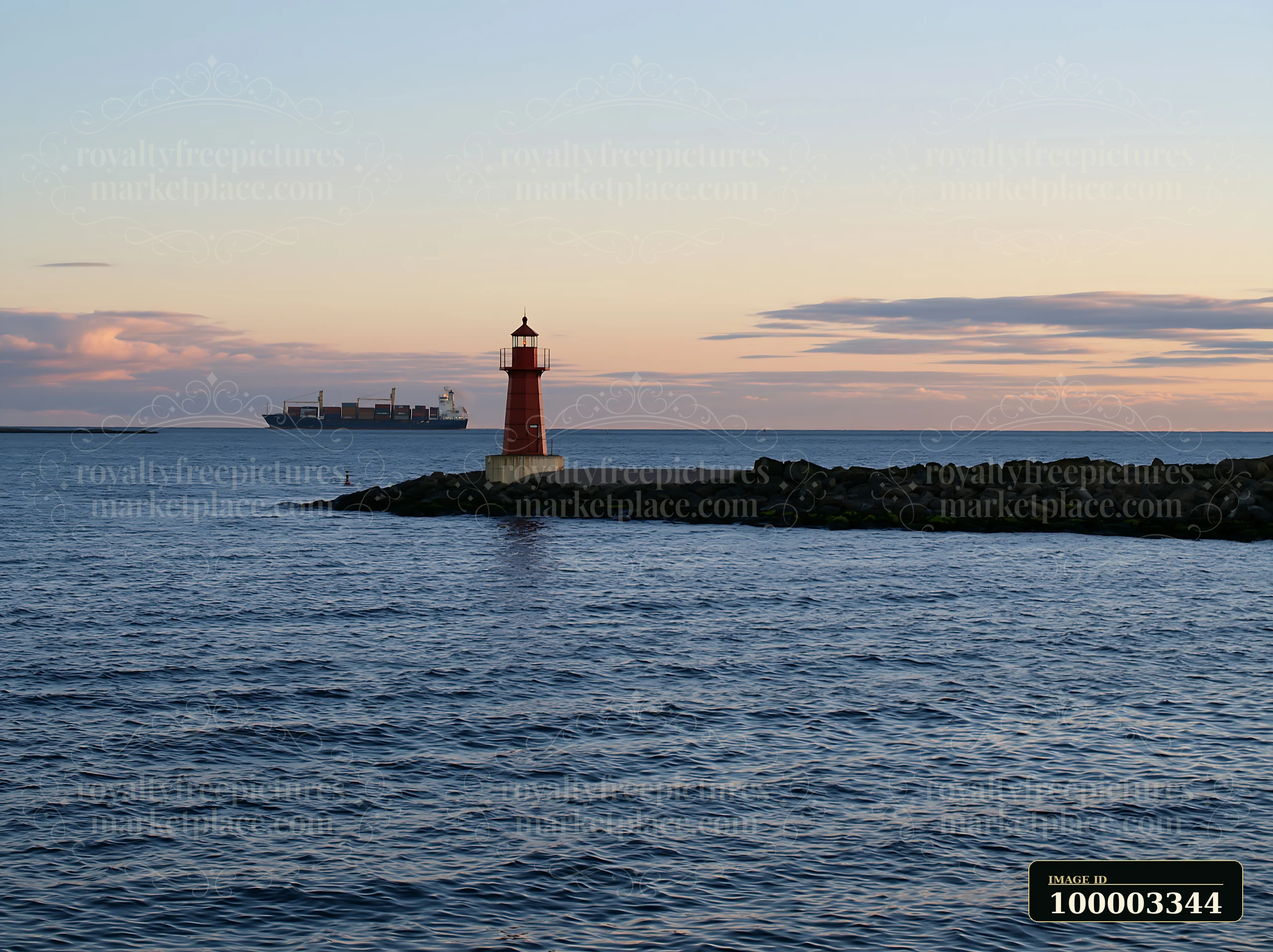 A lighthouse stands on a rocky shore with a cargo ship visible in the water at sunset.