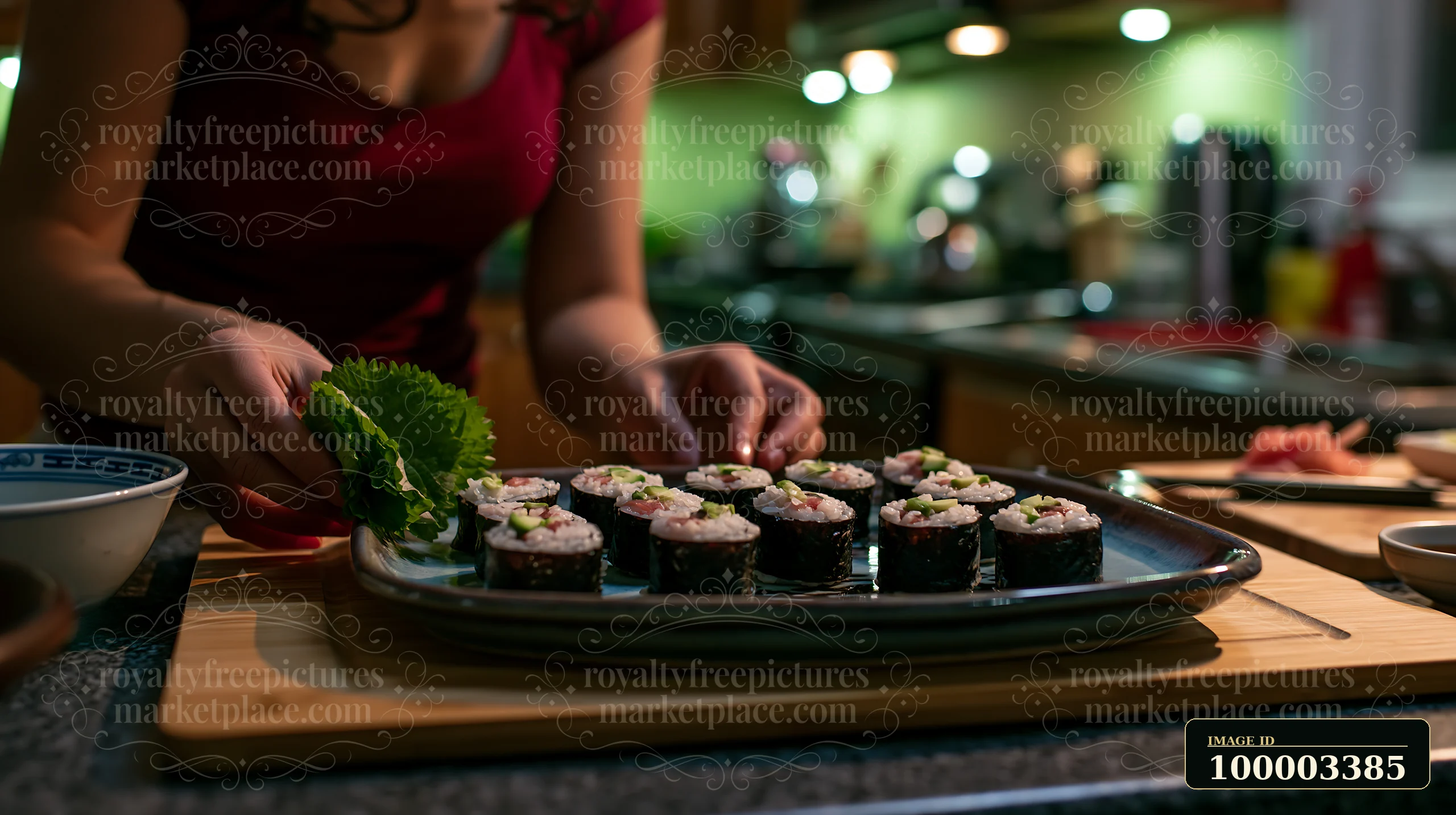 A person carefully arranges sushi with shiso leaves on a plate in a kitchen.