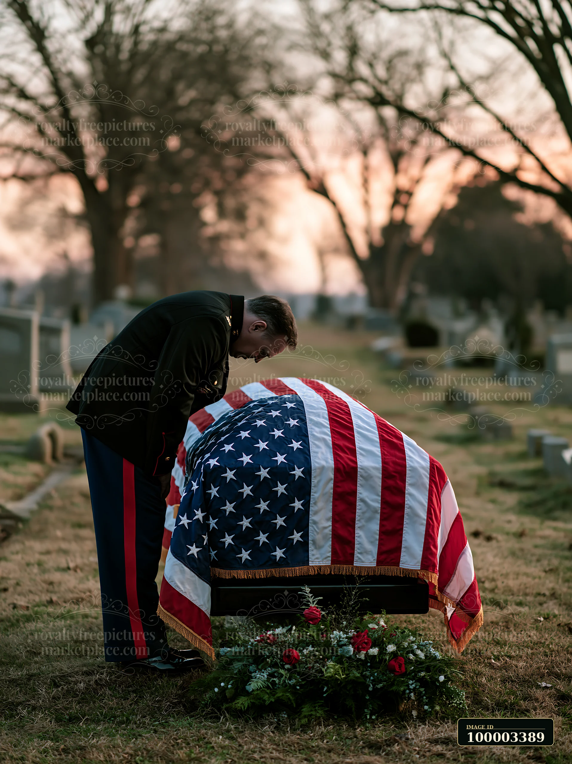 A man bows his head in respect at a burial site in a cemetery during sunset.