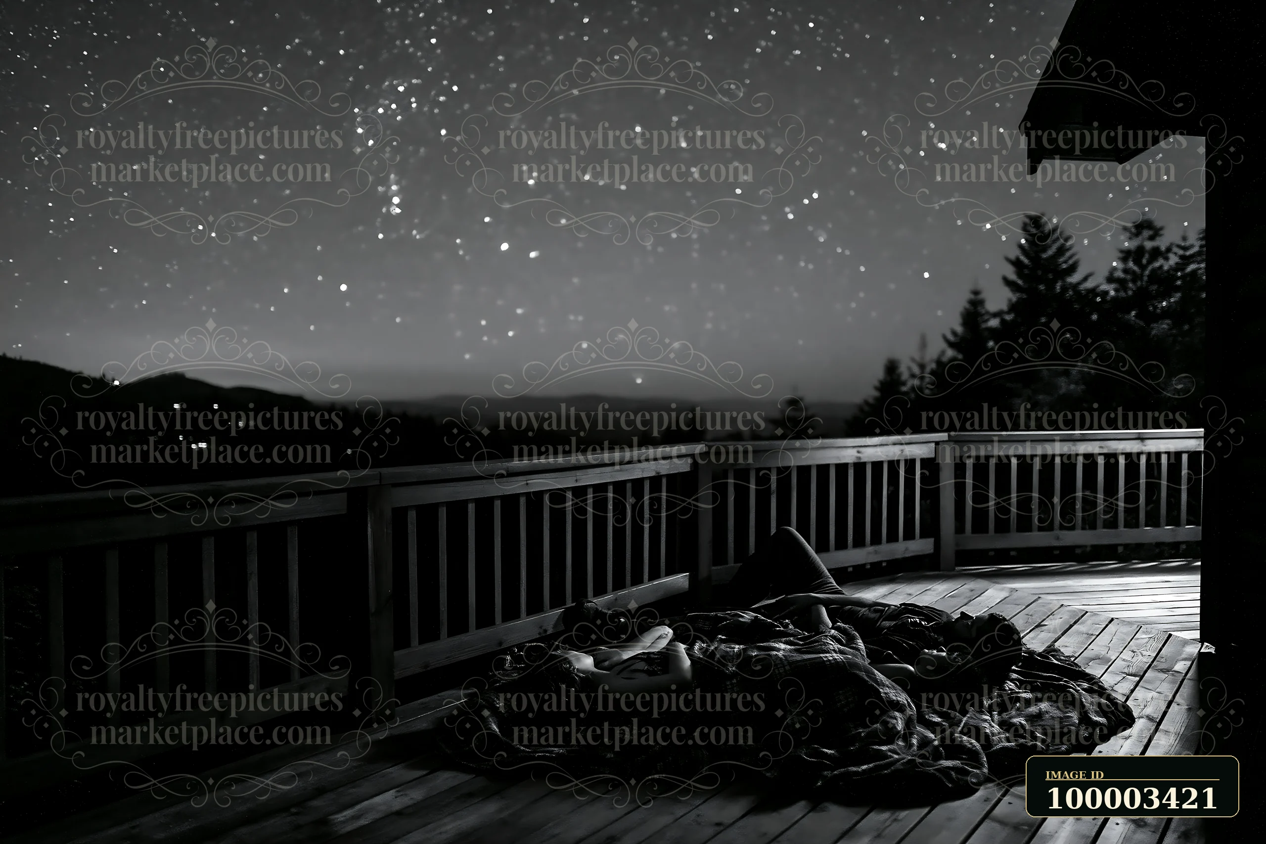 A couple lying on a blanket beneath stars on a wooden deck in a remote area.