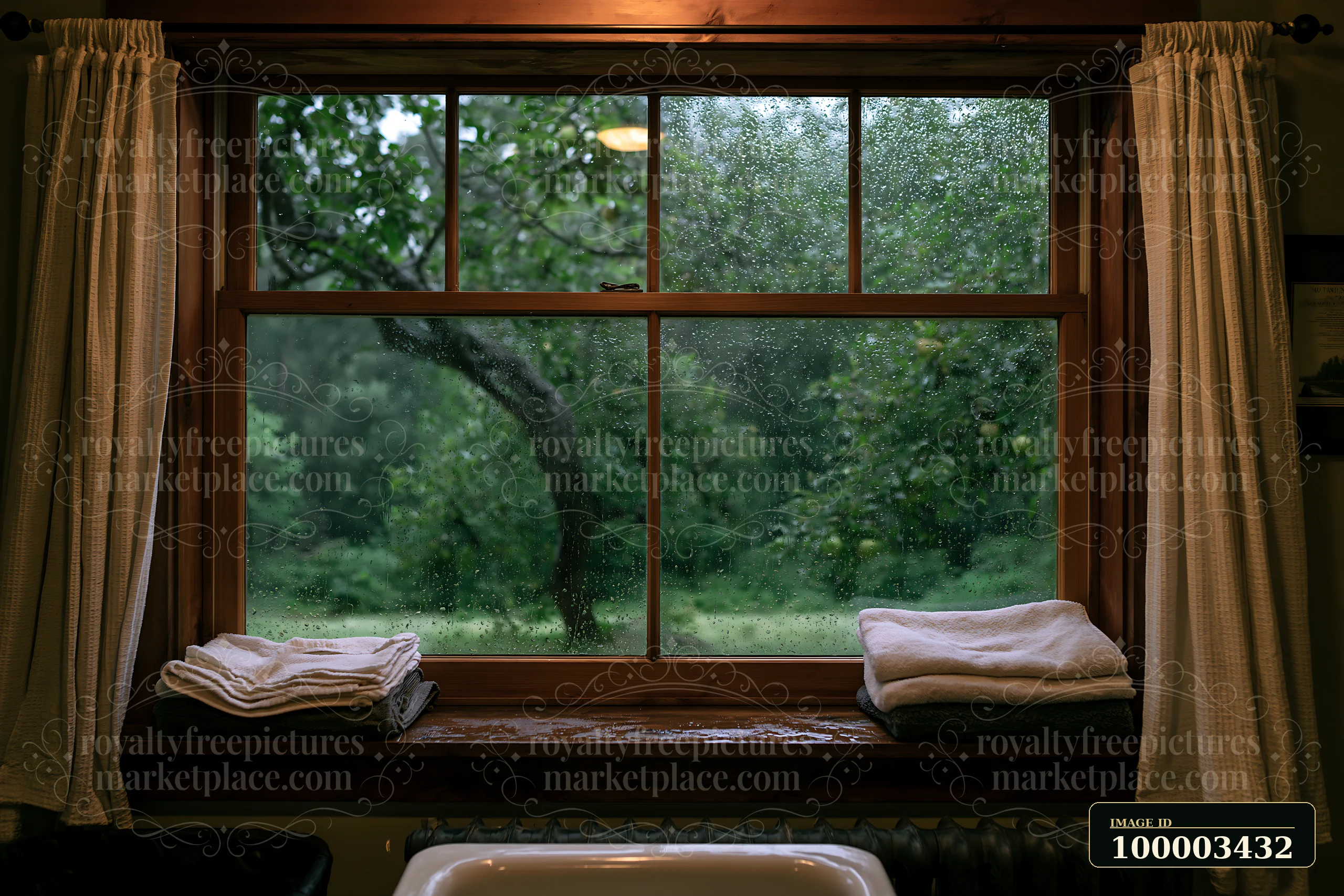 A rain-soaked wooden window in rural home features clean towels on the sill, with a blurred view of trees and grass outside.