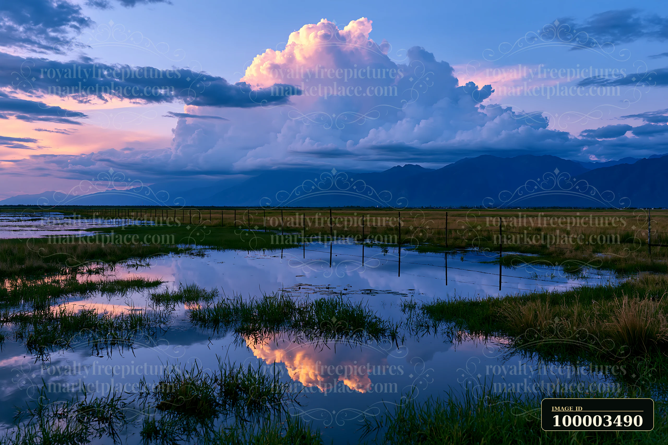 Dark clouds gather above a mountain range as colors reflect in a nearby water body.