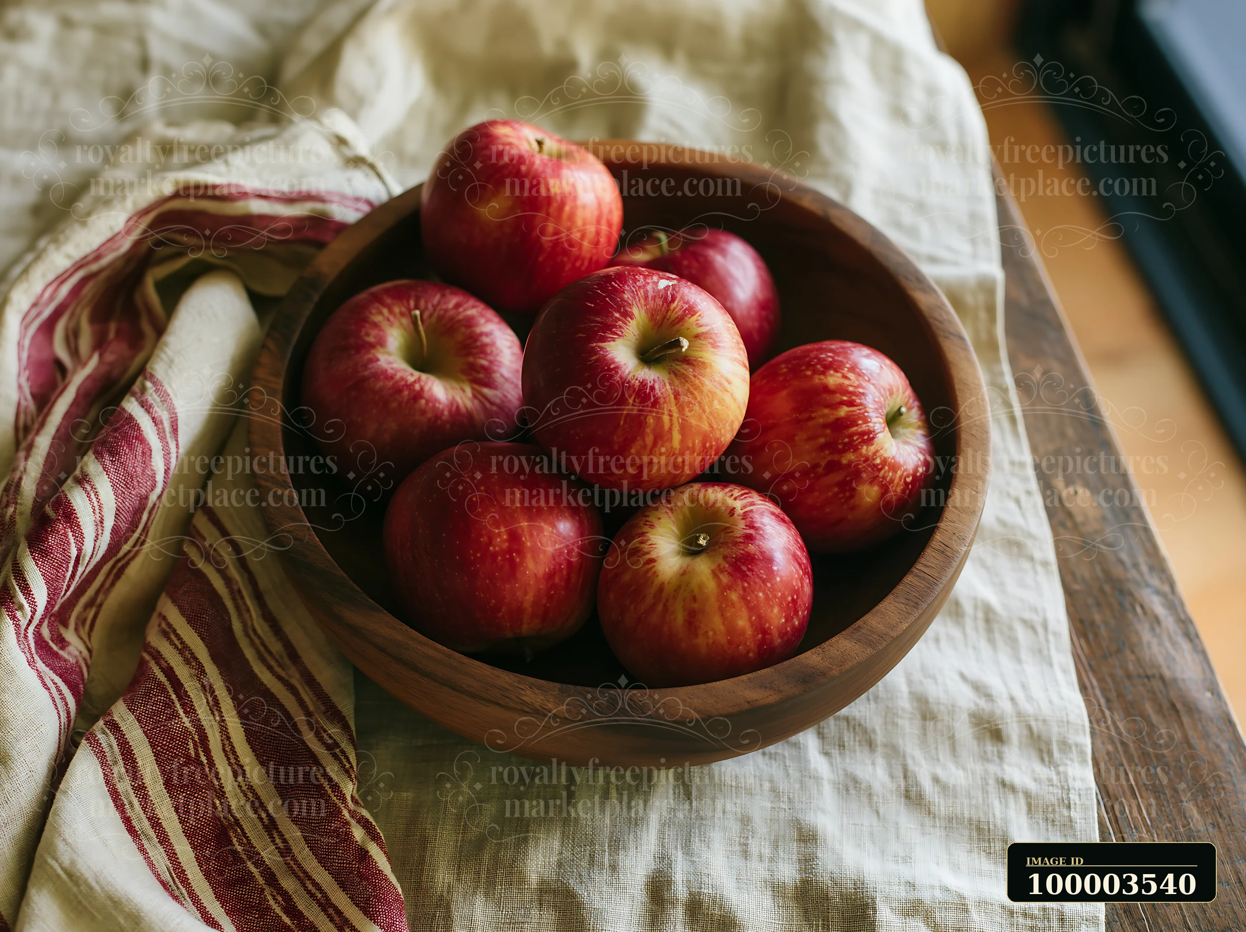 Red apples are arranged in a wooden bowl placed on a stained handmade linen tablecloth.