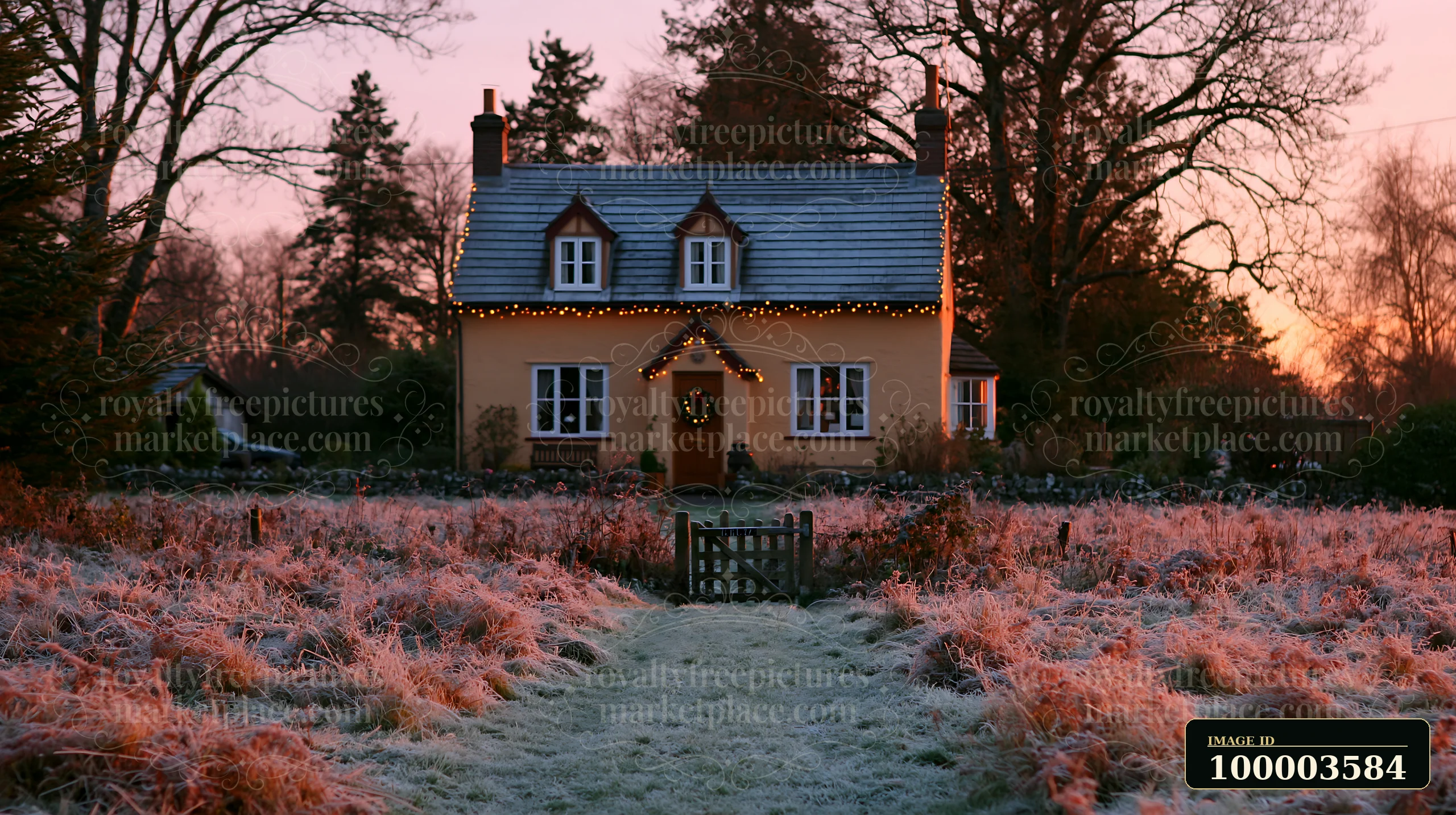 A cozy country cottage with Christmas decorations stands amidst frosty grass at sunset.