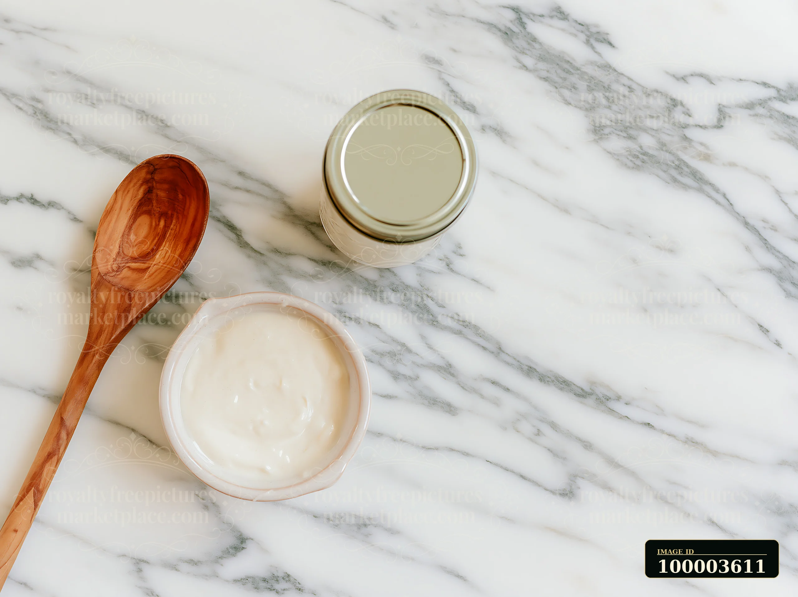 A cream dose sits in a small bowl on a marble countertop, next to a wooden spoon and a jar.