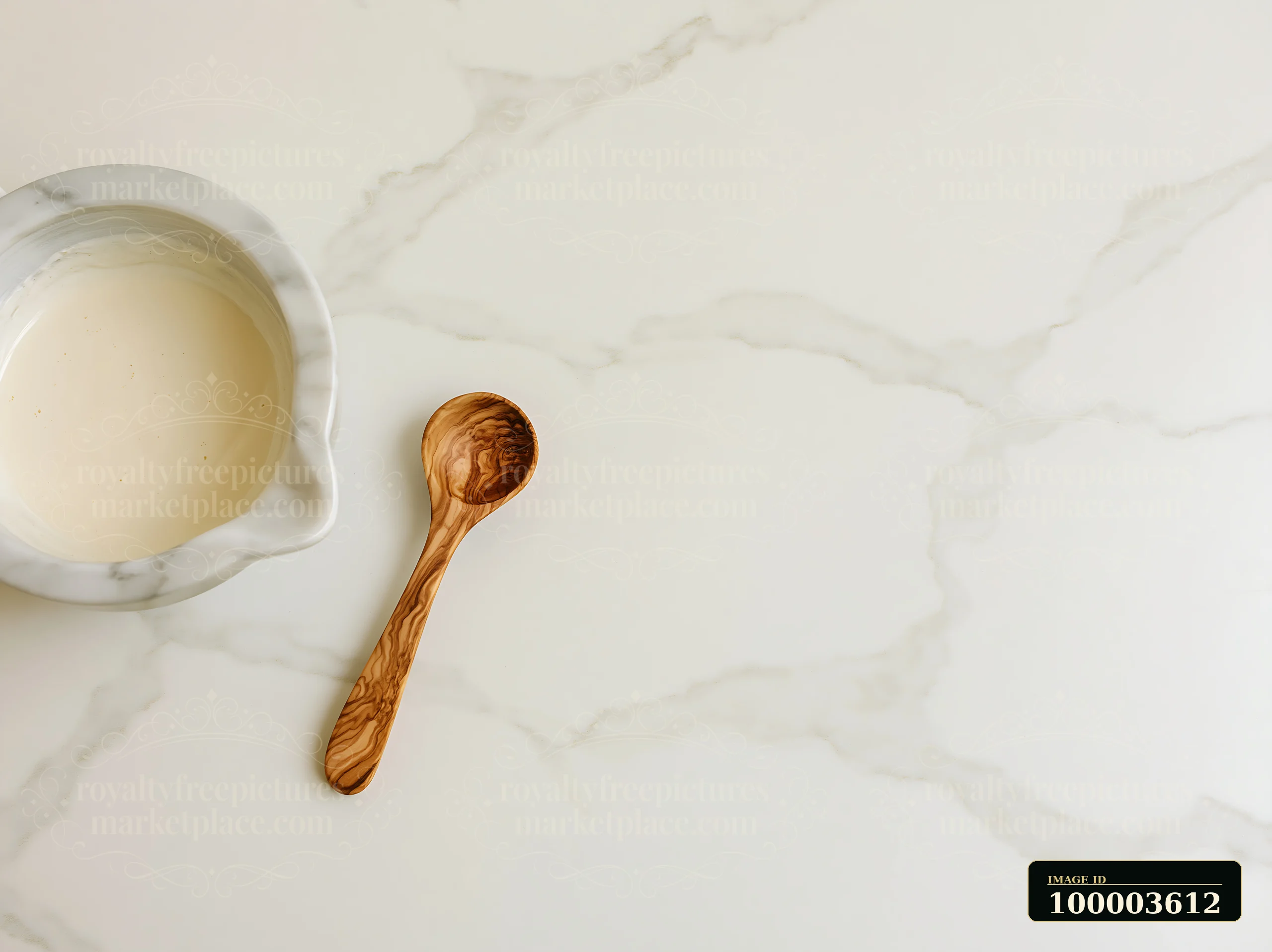 A bowl containing cream sits on a marble countertop with a wooden spoon nearby.