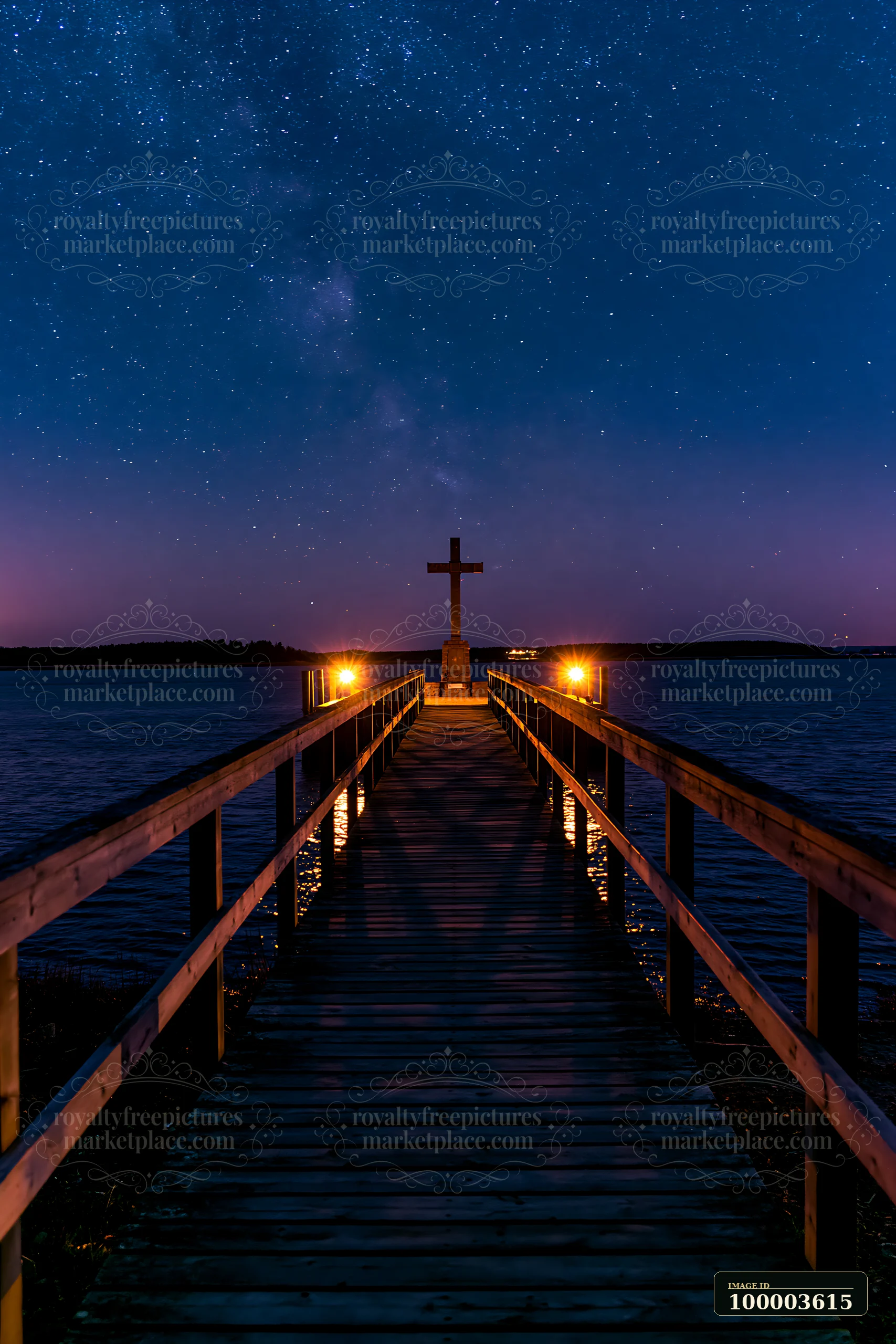A wooden pier leads to a war memorial cross silhouetted against stars in the night sky.