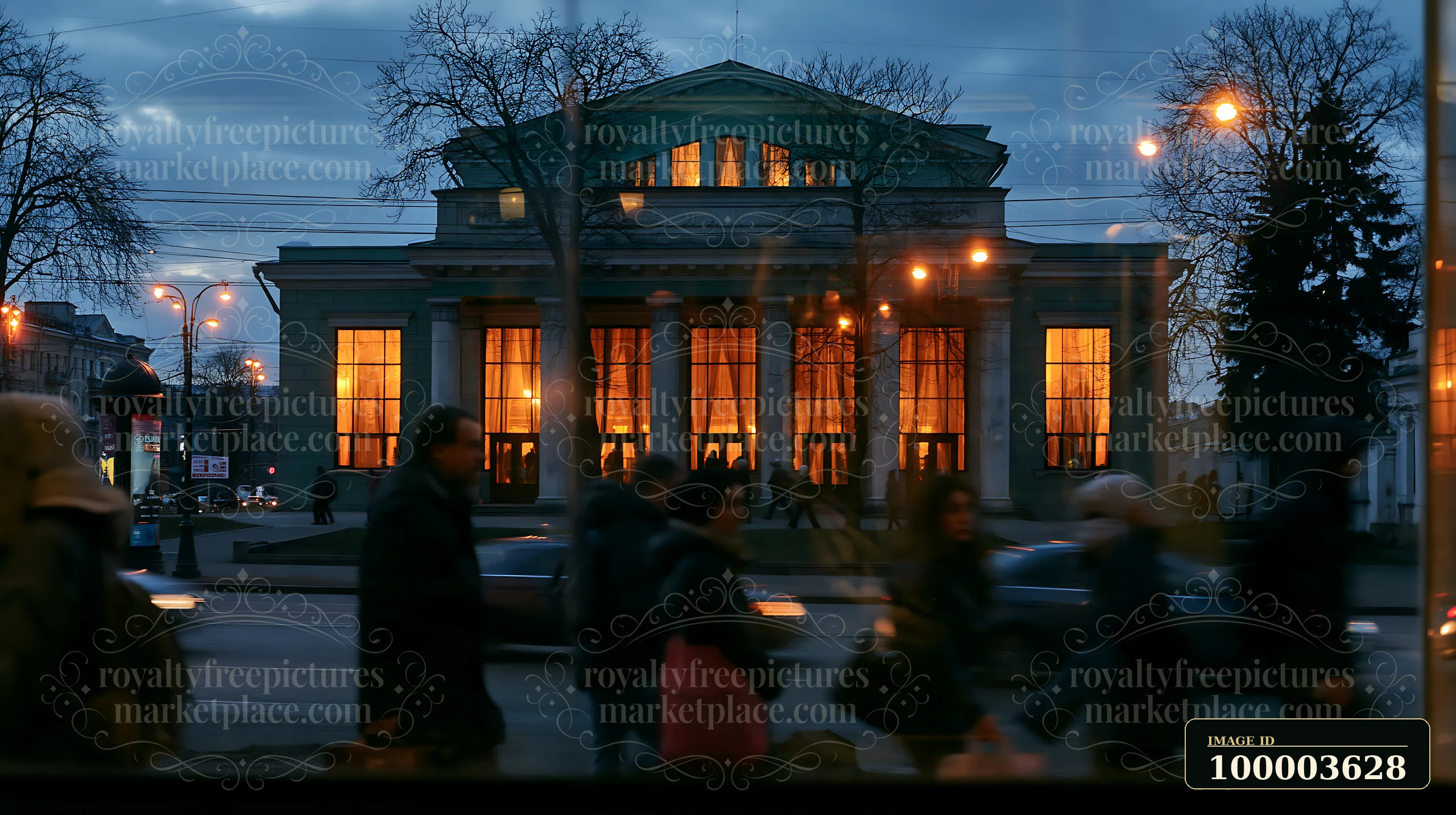 People walk by a Soviet theater exterior as warm light shines from its windows during dusk.
