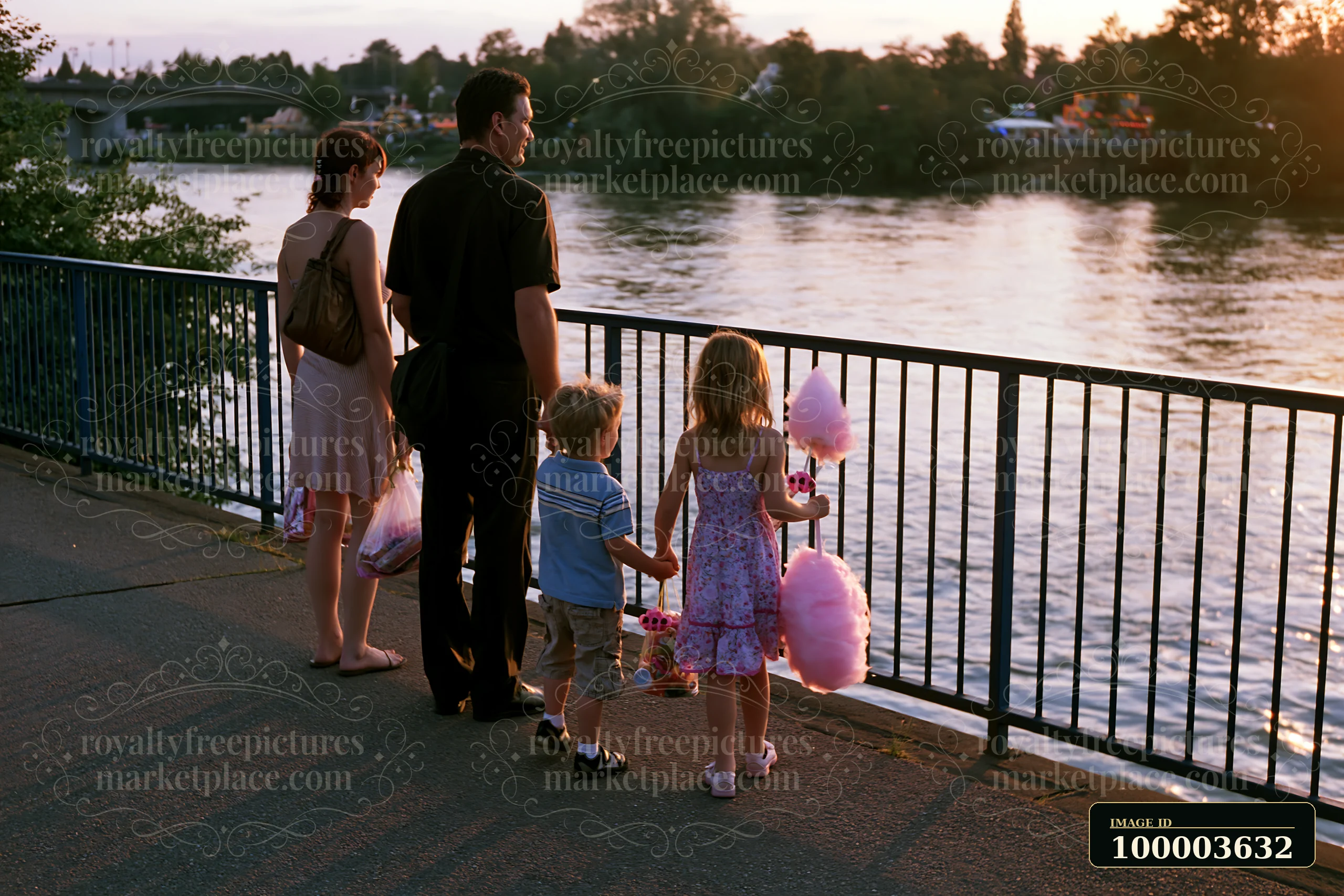 Family walking beside a river at sunset, with children carrying cotton candy and fair prizes.