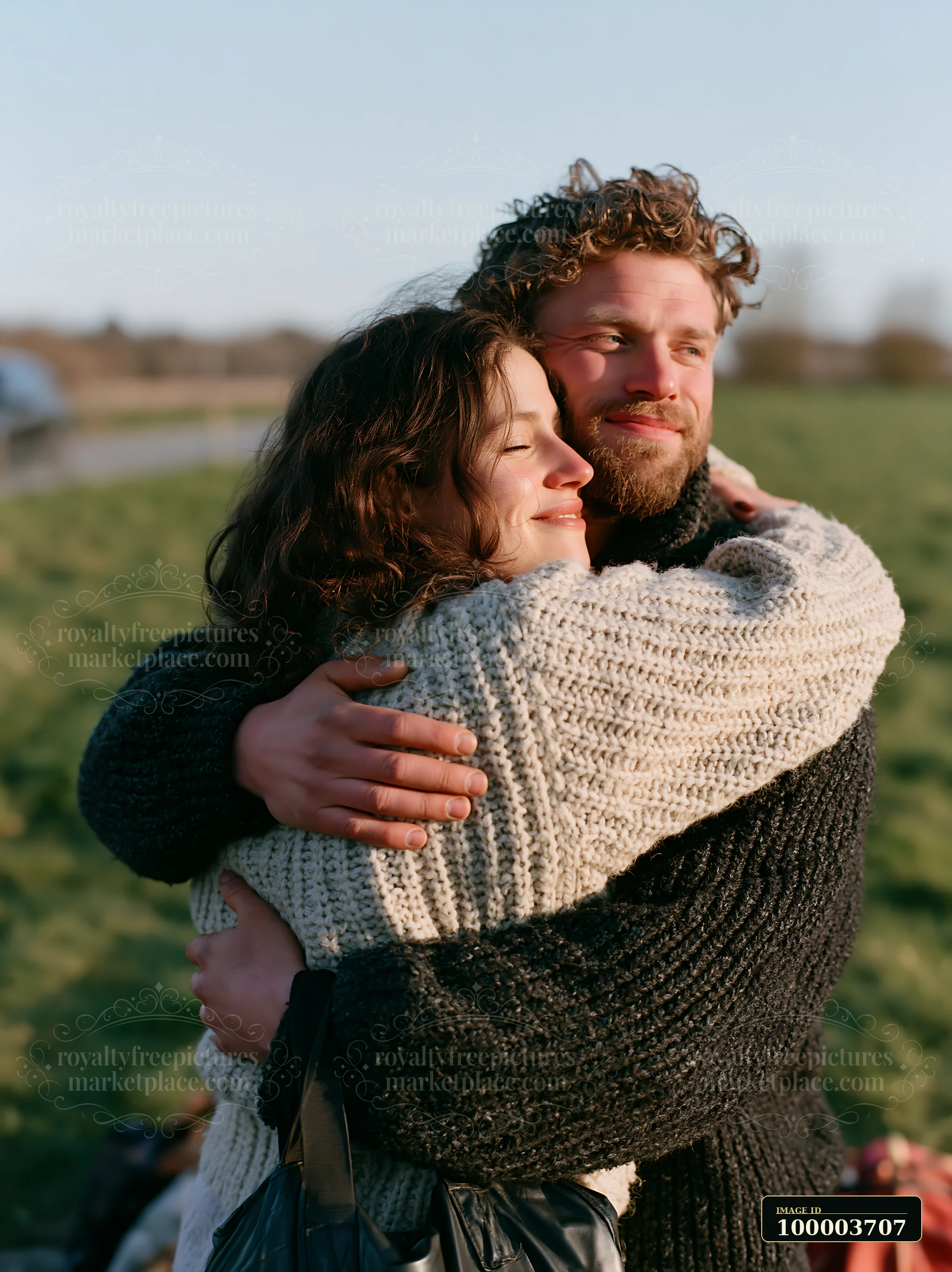 A couple is embracing outdoors in a grassy field with a blue sky in spring.