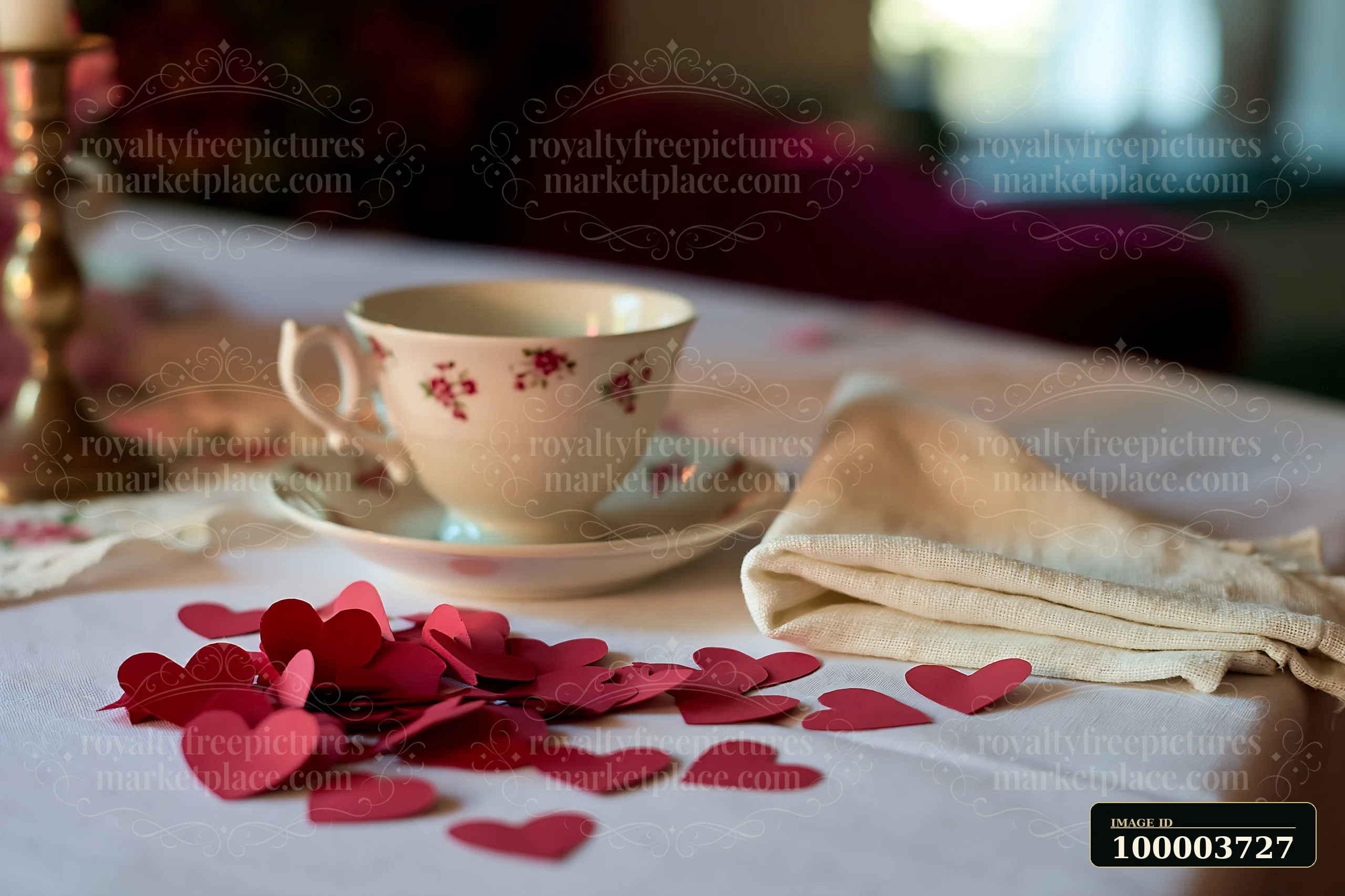 Red paper hearts lie scattered on a white table beside a floral teacup, saucer, and folded cloth napkin.