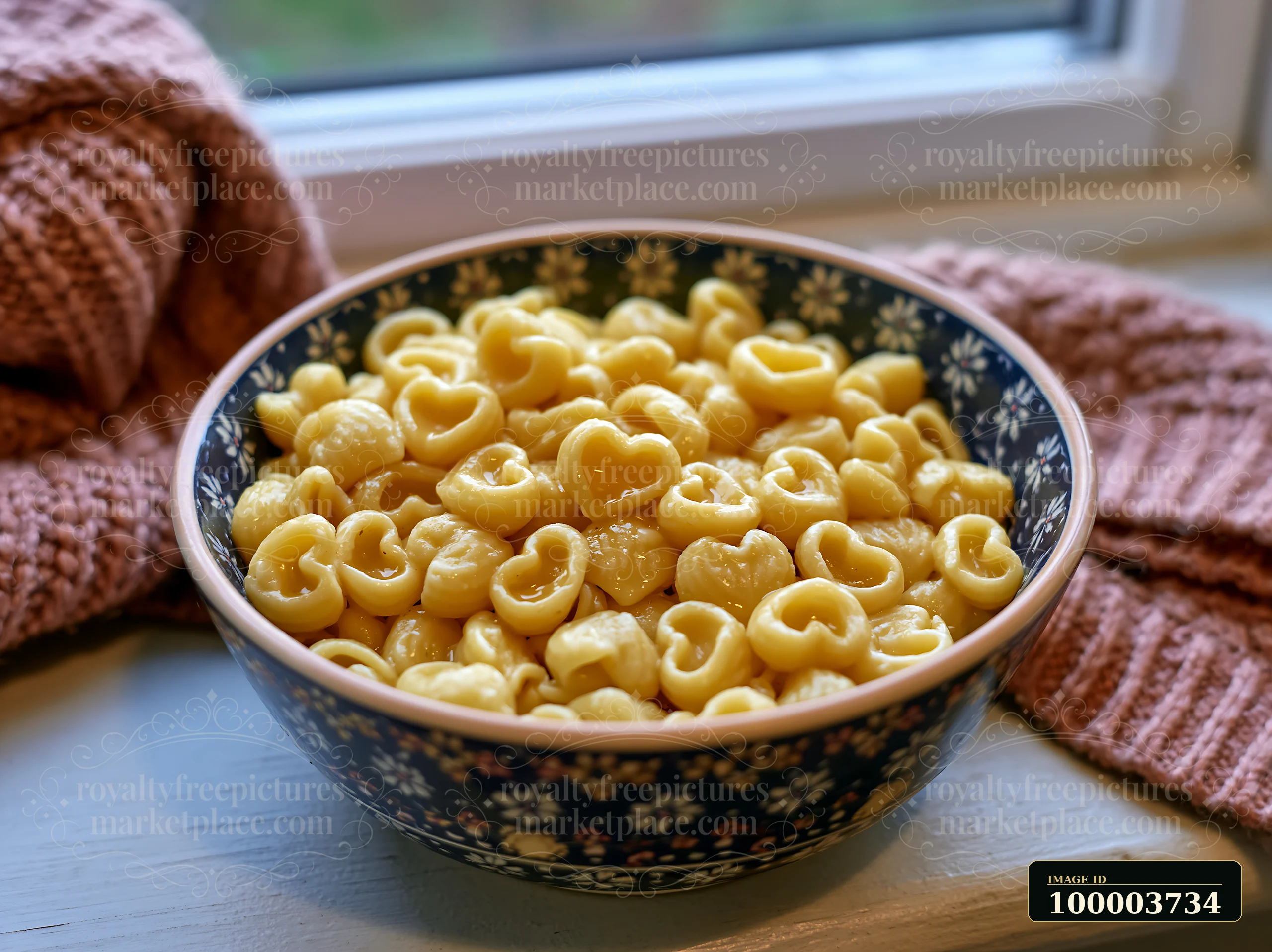 Heart-shaped pasta fills a bowl placed on a window sill next to a knitted blanket.