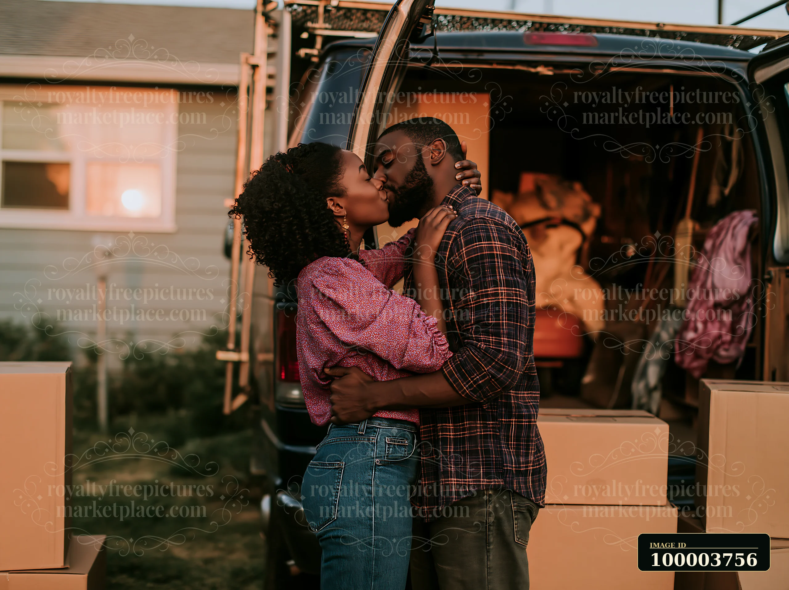 A couple shares a romantic kiss outside a moving van filled with boxes during sunset.