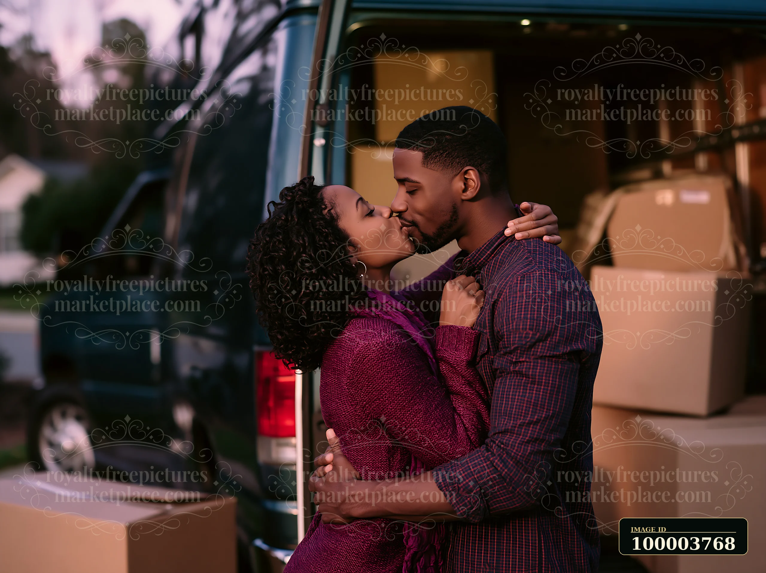 A couple leans in for a romantic kiss while surrounded by moving boxes in front of a van.
