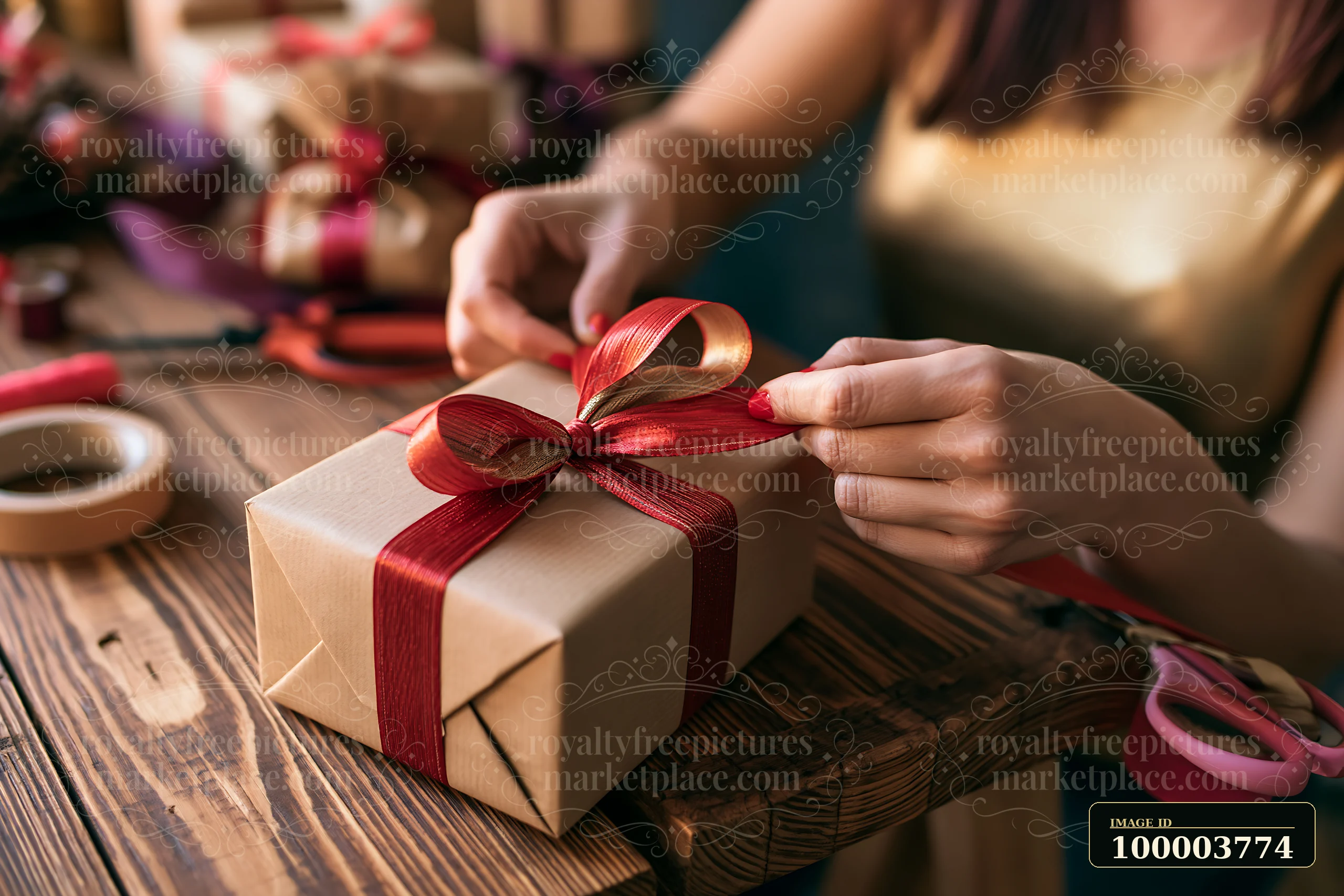 Hands tie a red ribbon around a kraft-wrapped gift box on a wooden table.