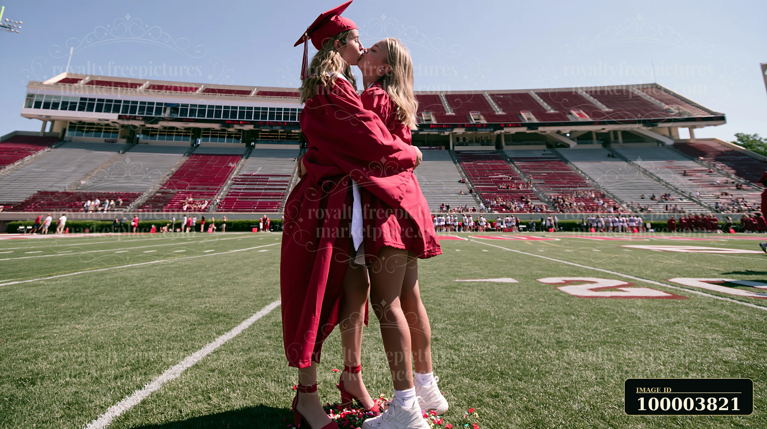 Two graduates kiss on the football field during a graduation celebration.