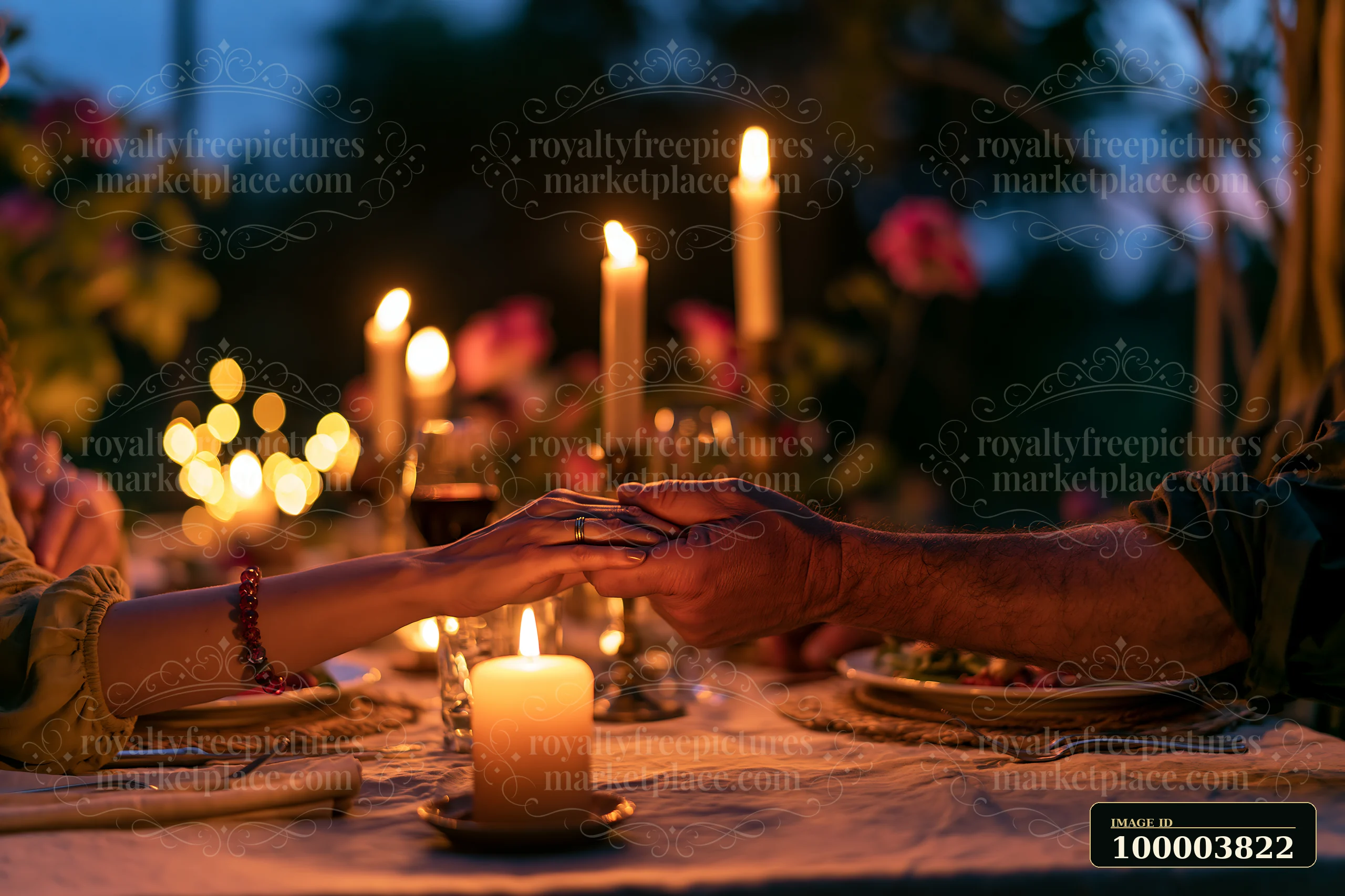 Two people hold hands across a candlelit dinner table surrounded by flowers.