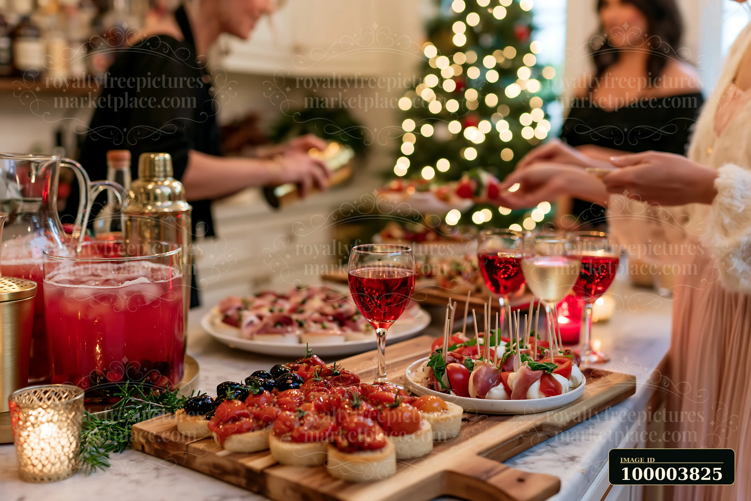 Appetizers on a wooden serving board with drinks and guests gathered beside a lit Christmas tree.