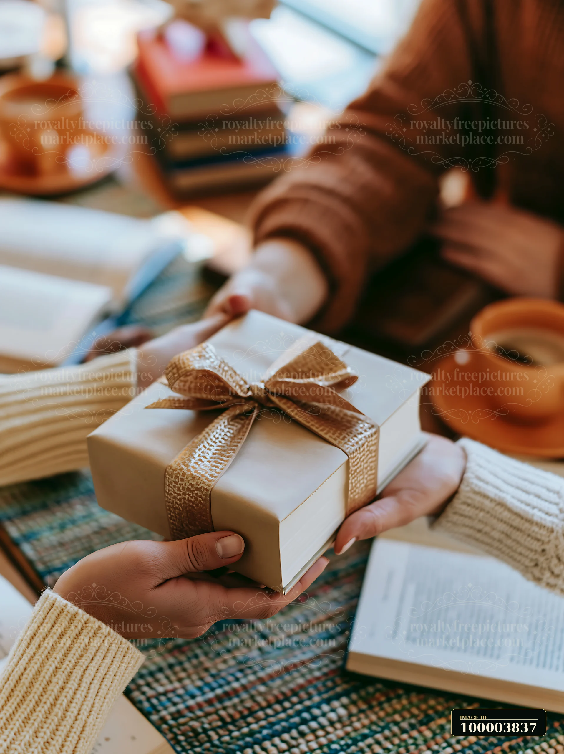 Two hands are exchanging a wrapped gift with a bow in a warm indoor setting filled with books and mugs.