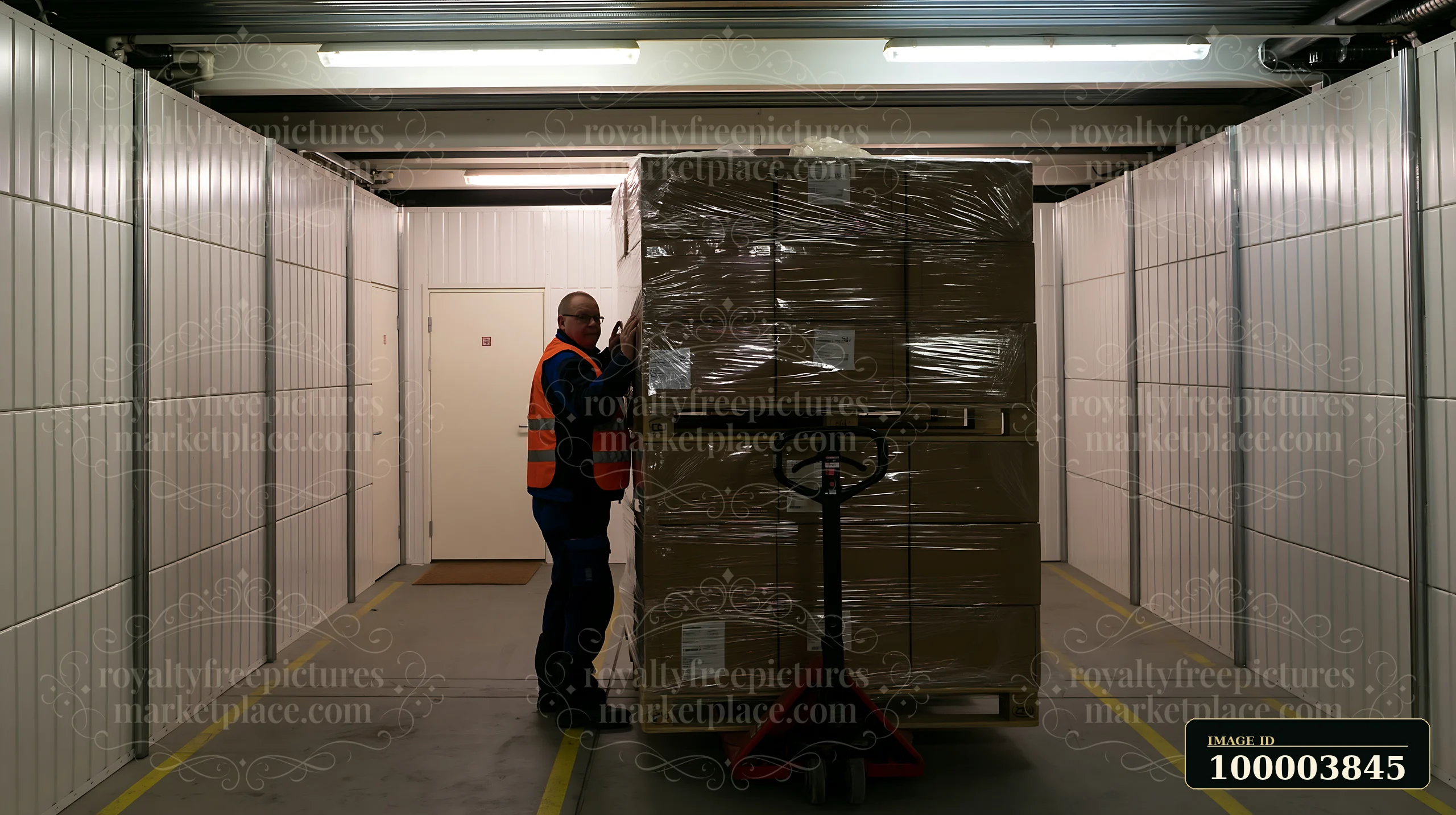 A worker moves a pallet of boxes within a storage unit aisle.
