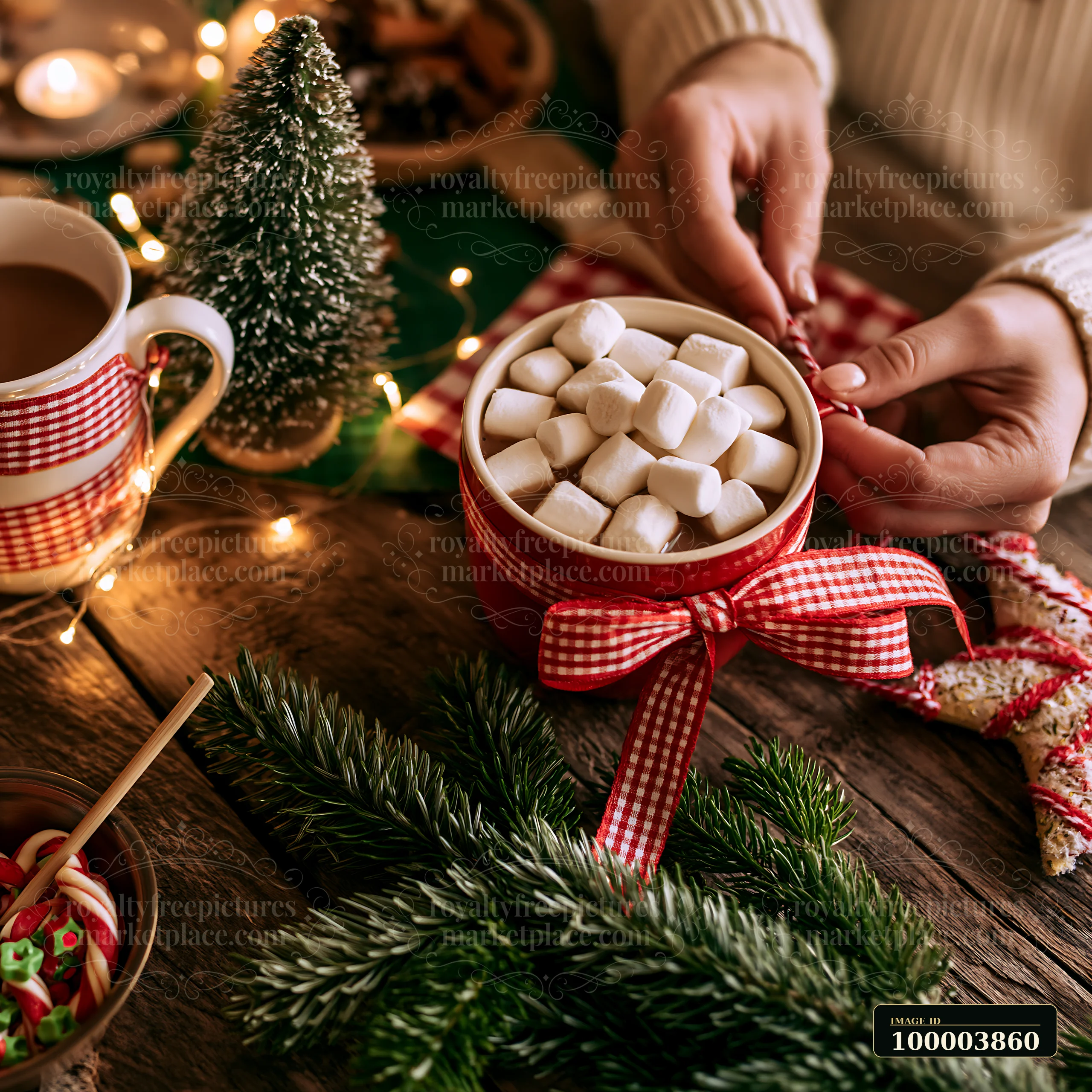 Mug of cocoa topped with marshmallows beside a miniature Christmas tree and festive ribbon on a wooden table.