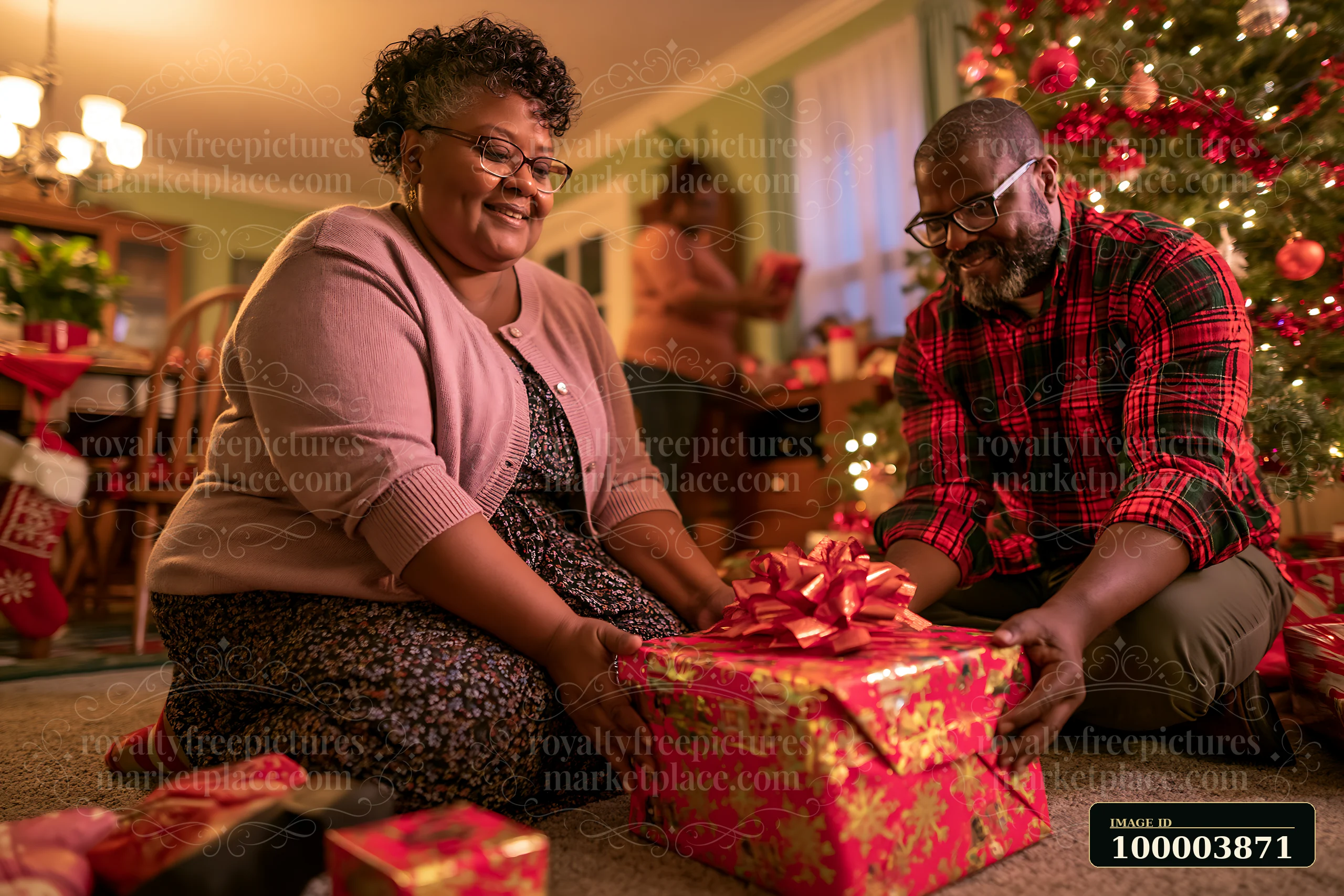 Two parents arrange wrapped gifts beside a decorated Christmas tree in a warmly lit living room.